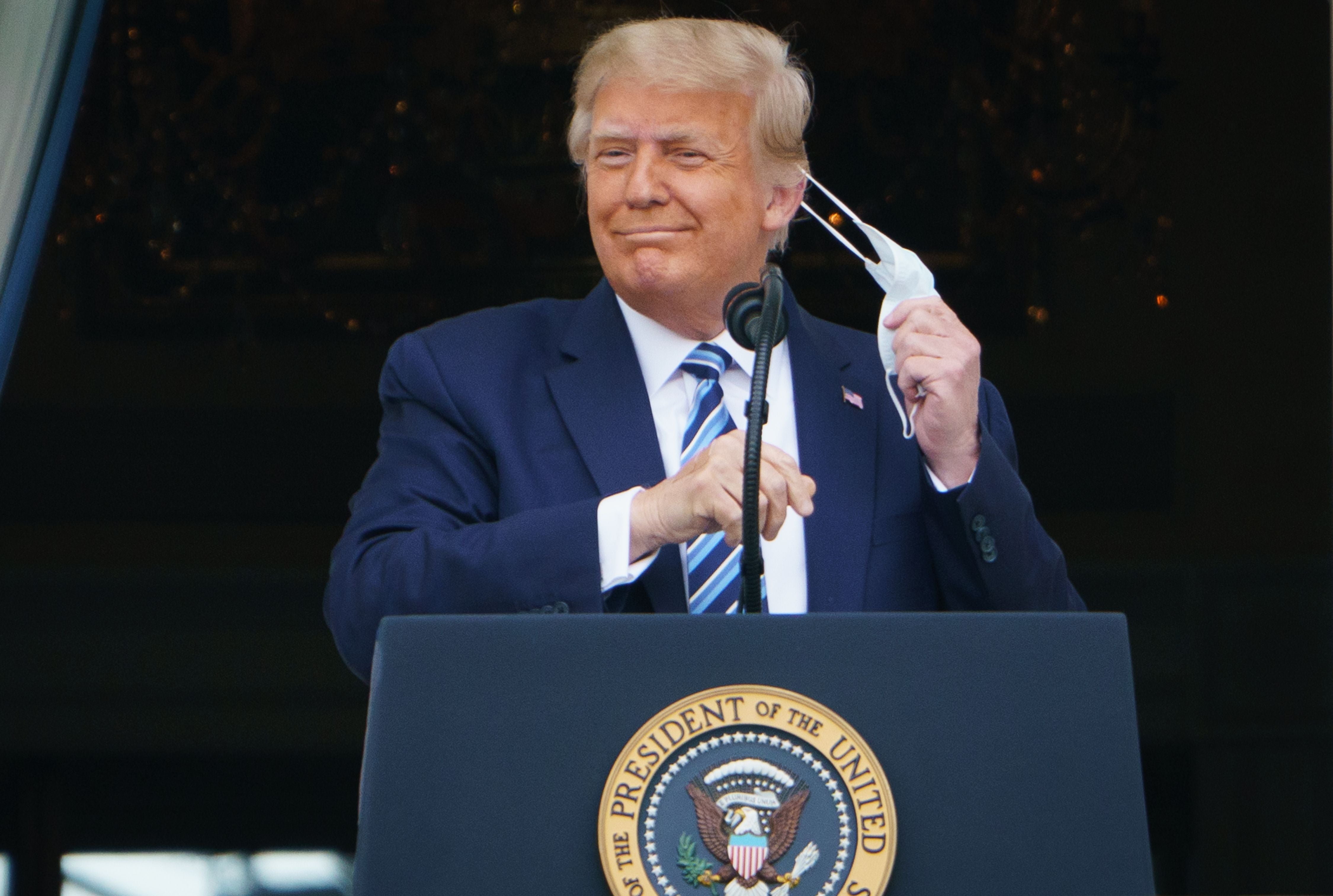 Donald Trump se quita la máscara antes de hablar desde el pórtico sur de la Casa Blanca en Washington, DC durante un mitin el 10 de octubre