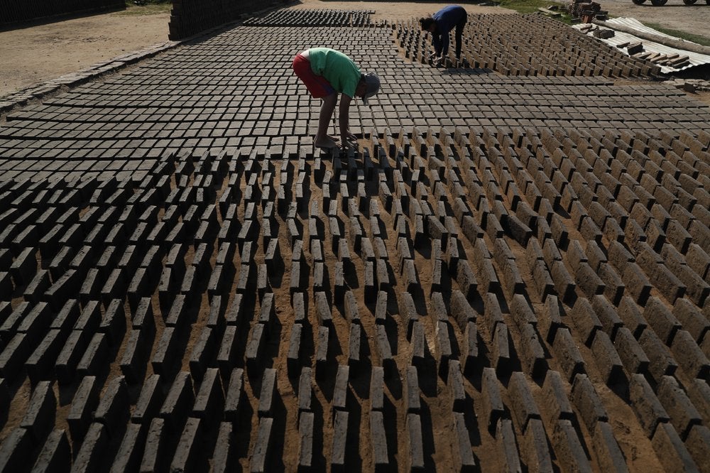 Cristian, al centro, voltea ladrillos de arcilla para que el sol los seque antes de que sean puestos en un horno en una pequeña fábrica en Tobati, Paraguay