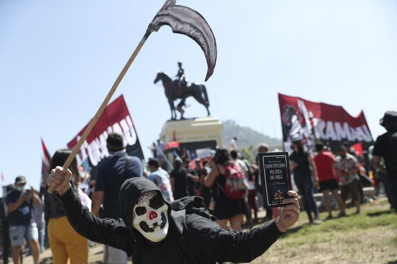 Un manifestante con una máscara sostiene la constitución de Chile mientras se manifiesta durante el primer aniversario del inicio de las protestas masivas contra el gobierno desencadenadas por el aumento de la tarifa del metro, que llevó a demandas por un cambio social en todo el país en Santiago de Chile, el domingo 18 de octubre del 2020. (Foto AP/Esteban Félix)