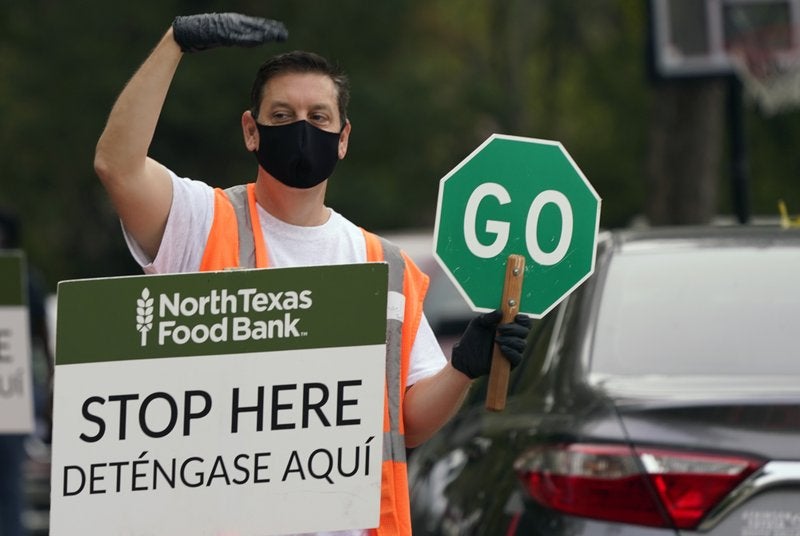 Usando una mascarilla como medida de prevención contra el nuevo coronavirus, el voluntario Michael Shearin ayuda a controlar el tránsito durante un evento de ayuda del banco de alimentos North Texas Food Bank el jueves 22 de octubre de 2020 en Dallas. (Foto/LM Otero)