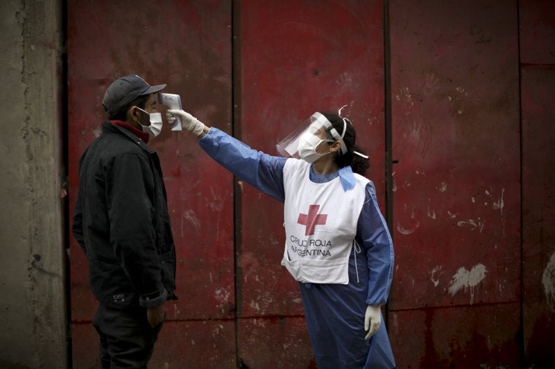 En esta imagen del 6 de junio de 2020, una voluntaria de la Cruz Roja le toma la temperatura a un hombre en el barrio de Fraga durante el cierre ordenado por el gobierno para frenar la propagación del nuevo coronavirus en Buenos Aires. (Foto/Natacha Pisarenko, Archivo)