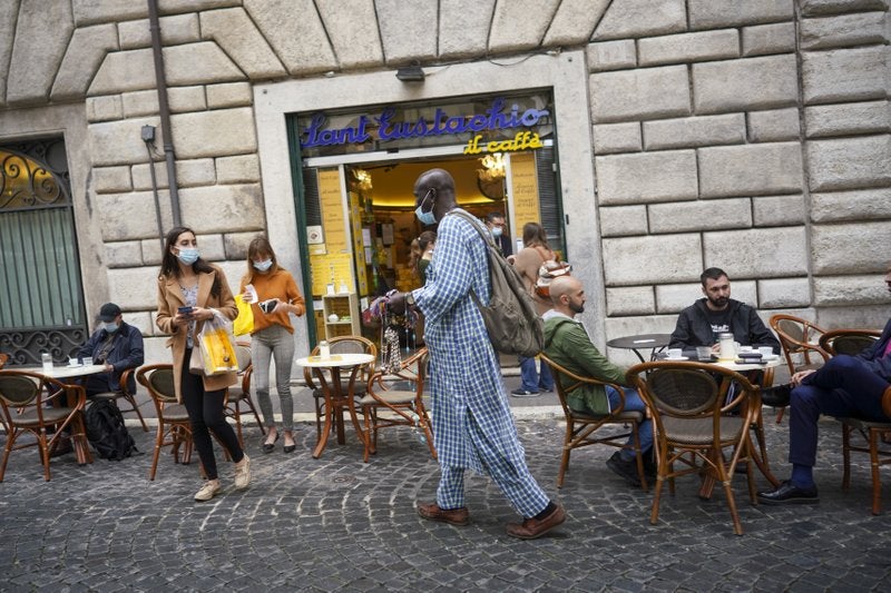 Un vendedor ambulante pasa frente a una cafetería en Roma.