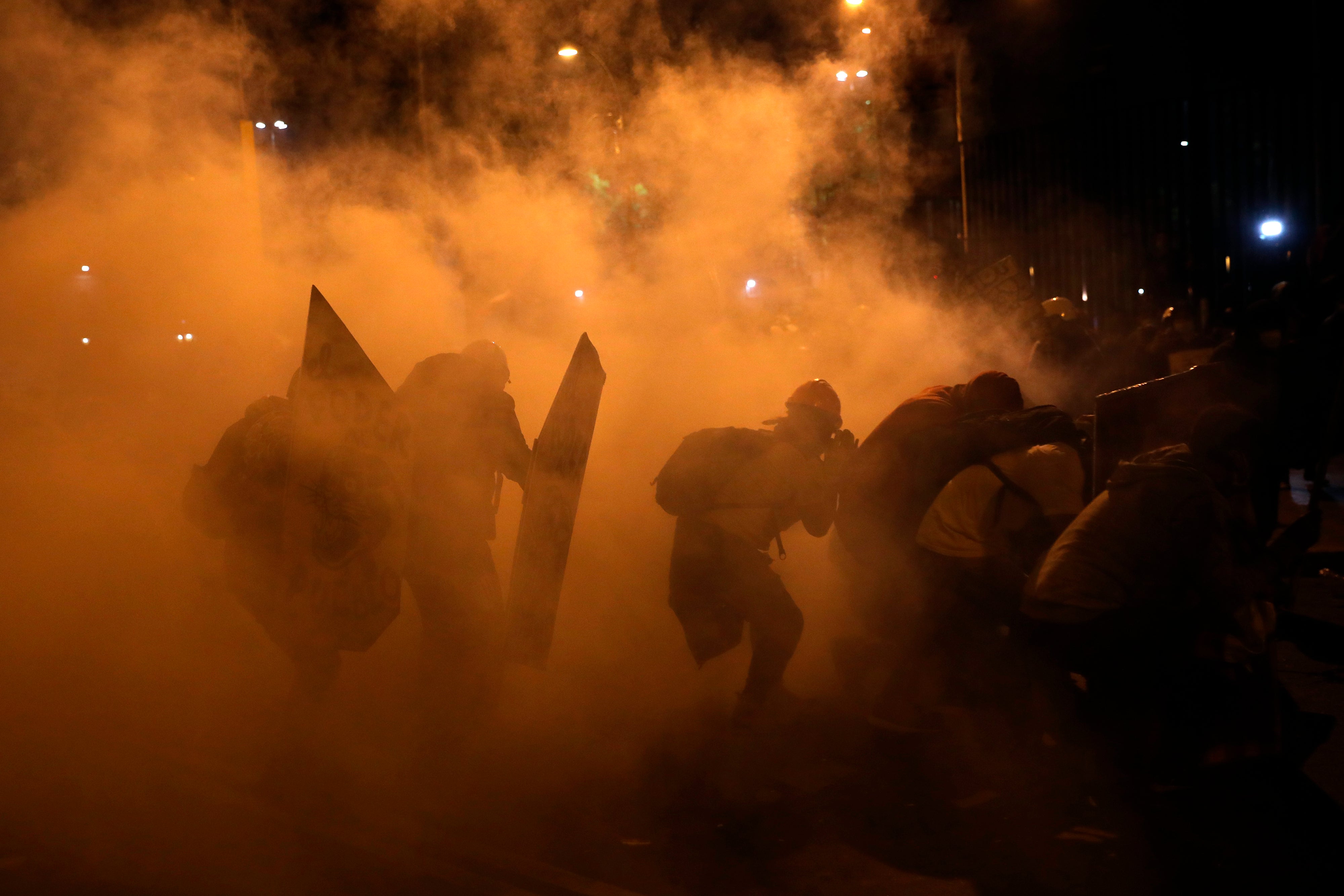 Manifestantes buscan resguardo del gas lacrimógeno lanzado por la policía para dispersar a los manifestantes reunidos en la Plaza San Martín en repudio del nuevo gobierno del presidente Manuel Merino, en Lima, el sábado 14 de noviembre de 2020.