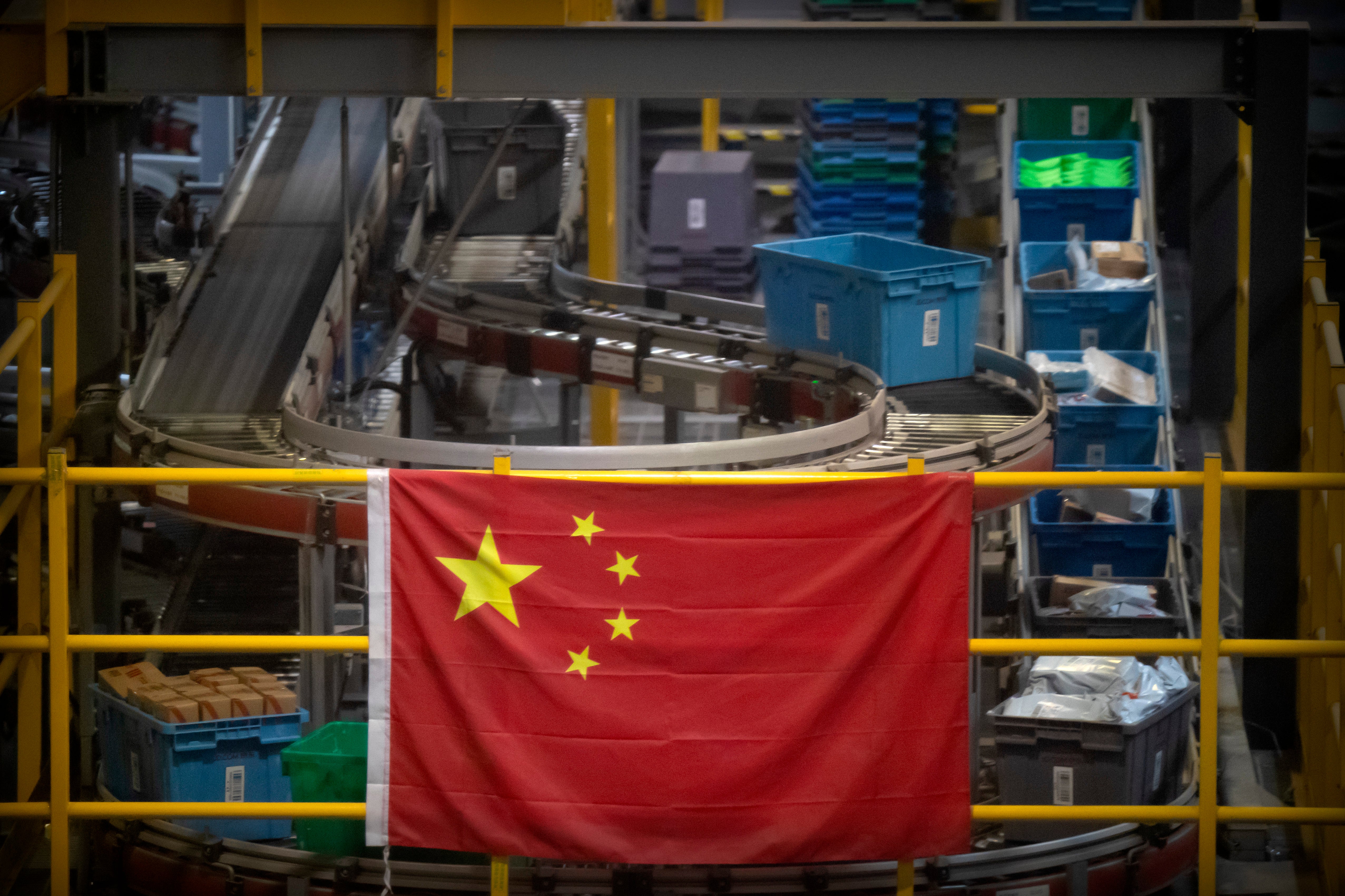 En esta fotografía de archivo del 11 de noviembre de 2020, una bandera china cuelga cerca de una línea de manejo de paquetes en un almacén de un minorista en línea en Beijing.&nbsp;