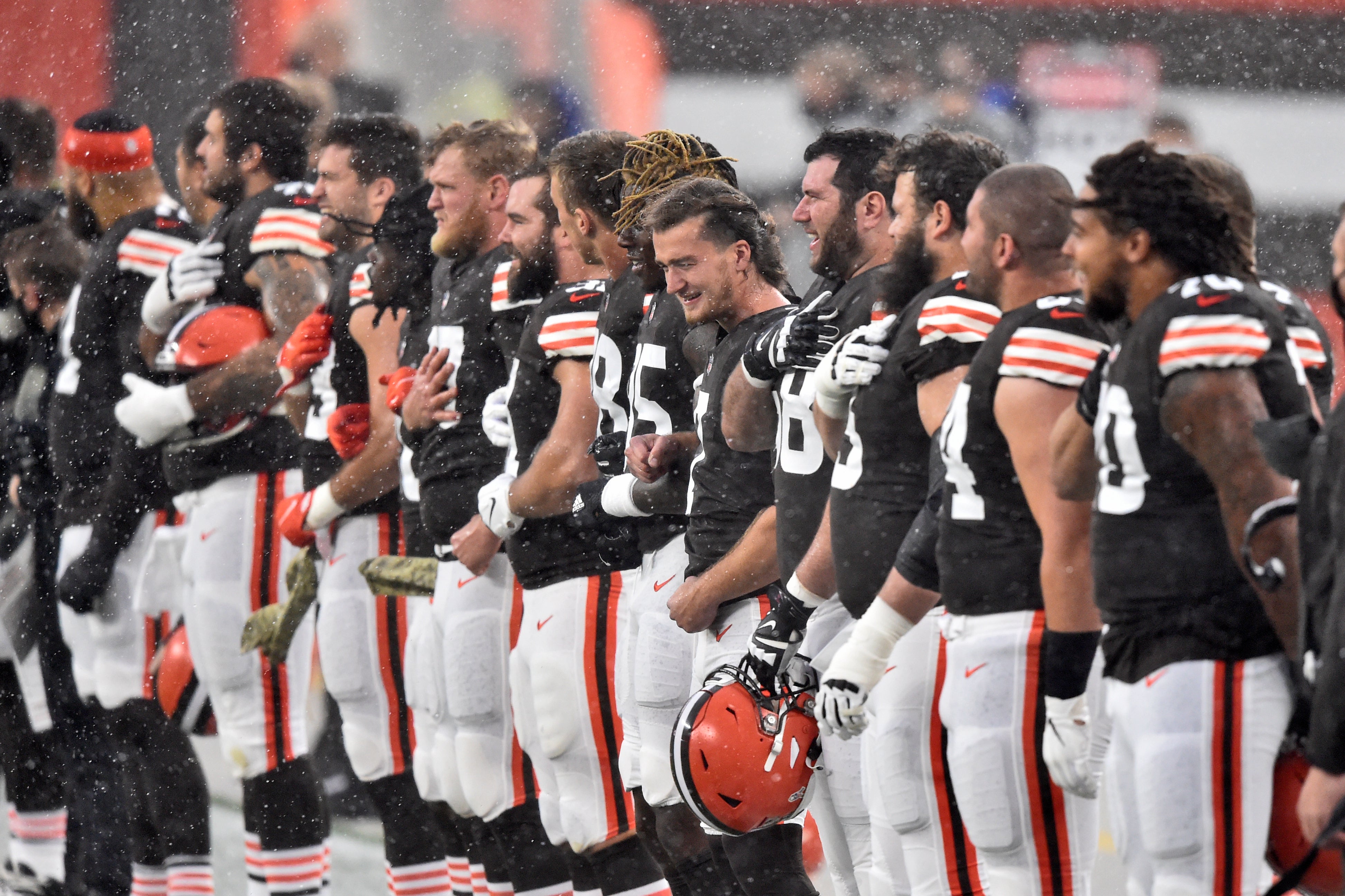 Jugadores de los Browns de Cleveland escuchan el himno nacional bajo la lluvia antes del partido frente a los Texans de Houston, el domingo 15 de noviembre de 2020, en Cleveland.