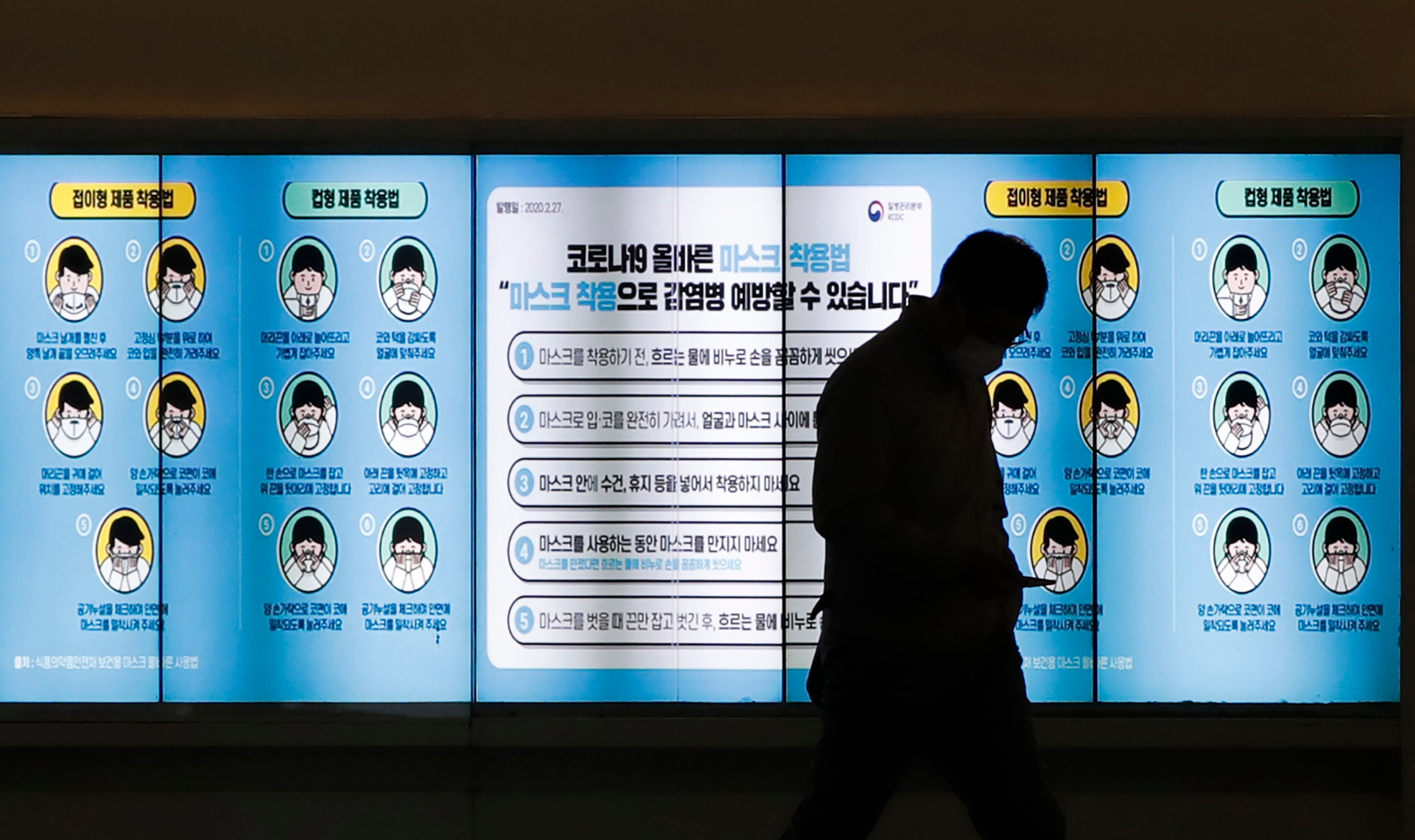 Un hombre con mascarilla pasa por delante de una pantalla que muestra las medidas de precaución contra el coronavirus, en Seúl, Corea del Sur, el 20 de noviembre de 2020. El letrero dice "Como llevar mascarilla".