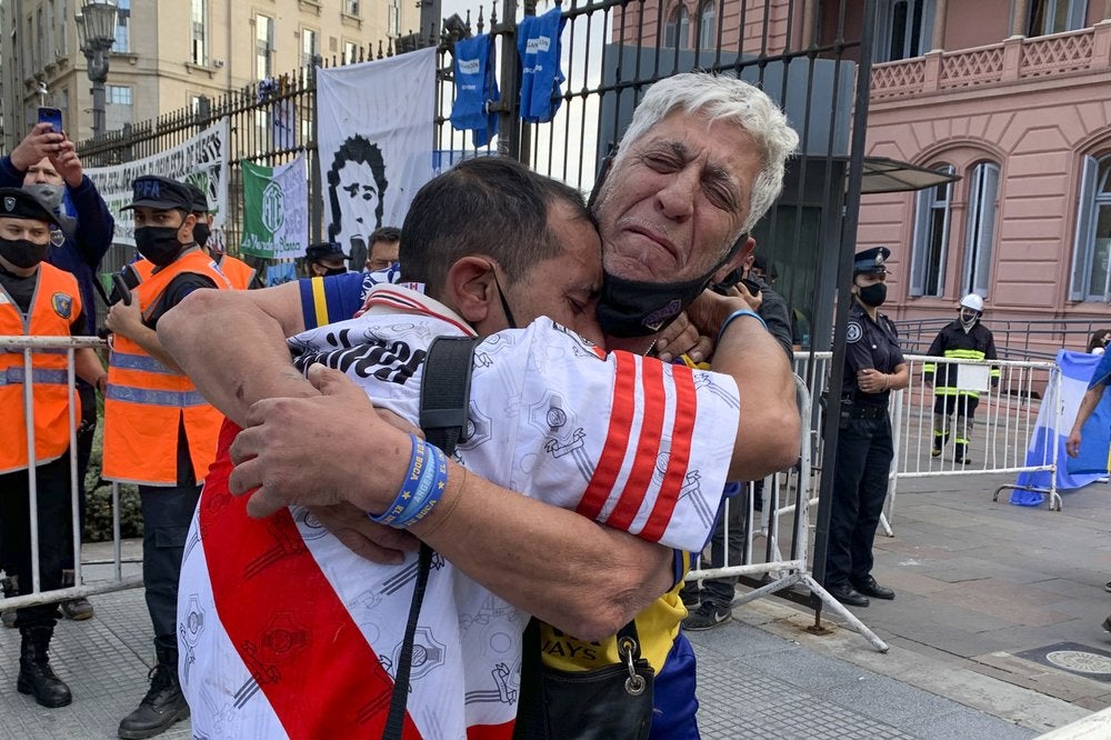 Hinchas de los clubes rivales Boca Juniors y River Plate se abrazan al esperar ingresar por ver el féretro que contiene el cuerpo de Diego.