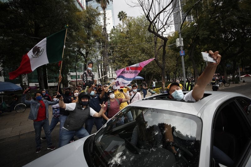 Un hombre posa desde su automóvil para una fotografía con aficionados que celebran la victoria del piloto mexicano.