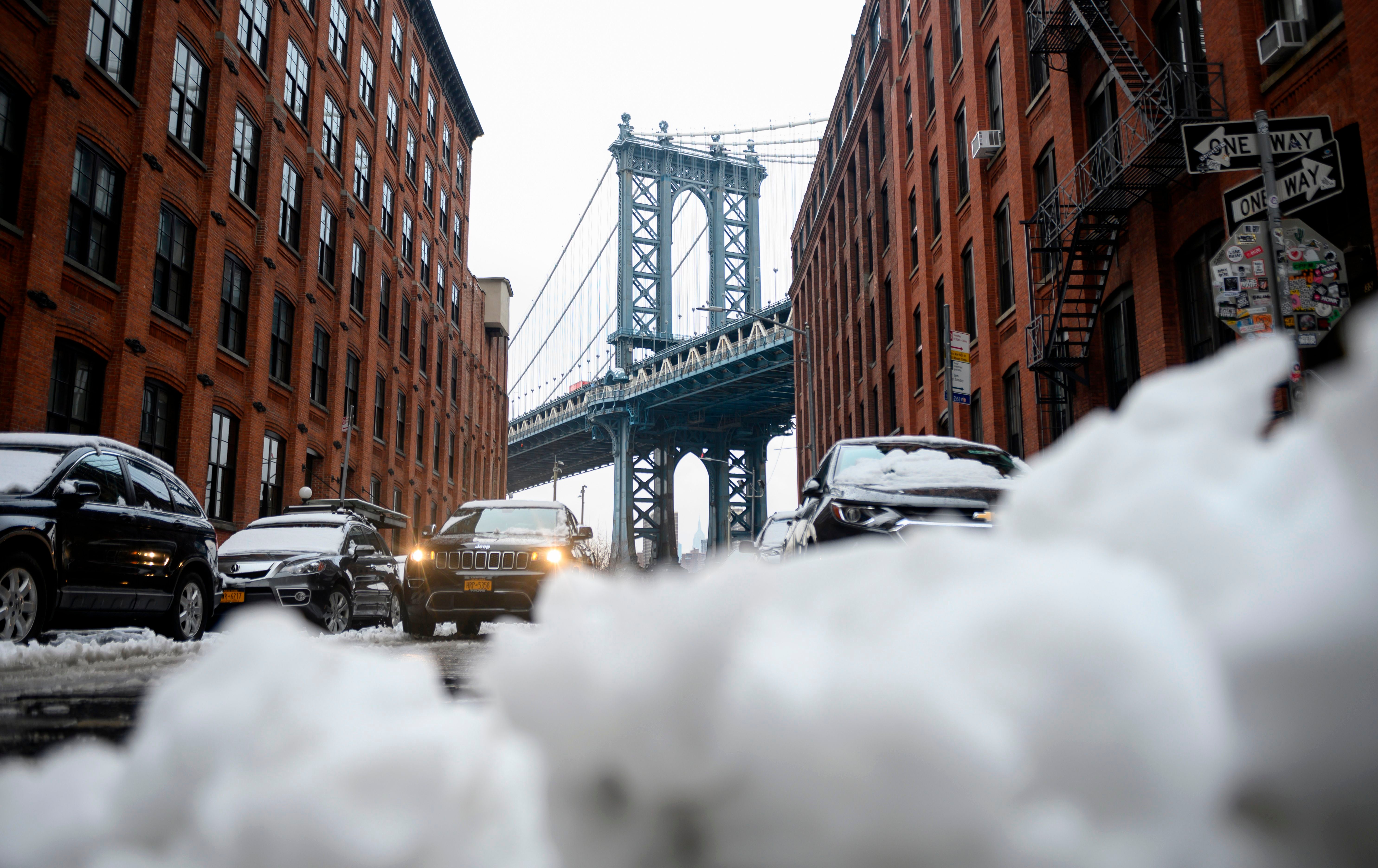 TOPSHOT - Se ve un automóvil junto a un montón de nieve frente al puente de Manhattan el 4 de marzo de 2019 en Nueva York, después de que una tormenta de nieve tardía en la temporada provocara que el alcalde de Nueva York, Bill de Blasio, anunciara el domingo por la tarde que las escuelas públicas de la ciudad de Nueva York estaría cerrado.&nbsp;