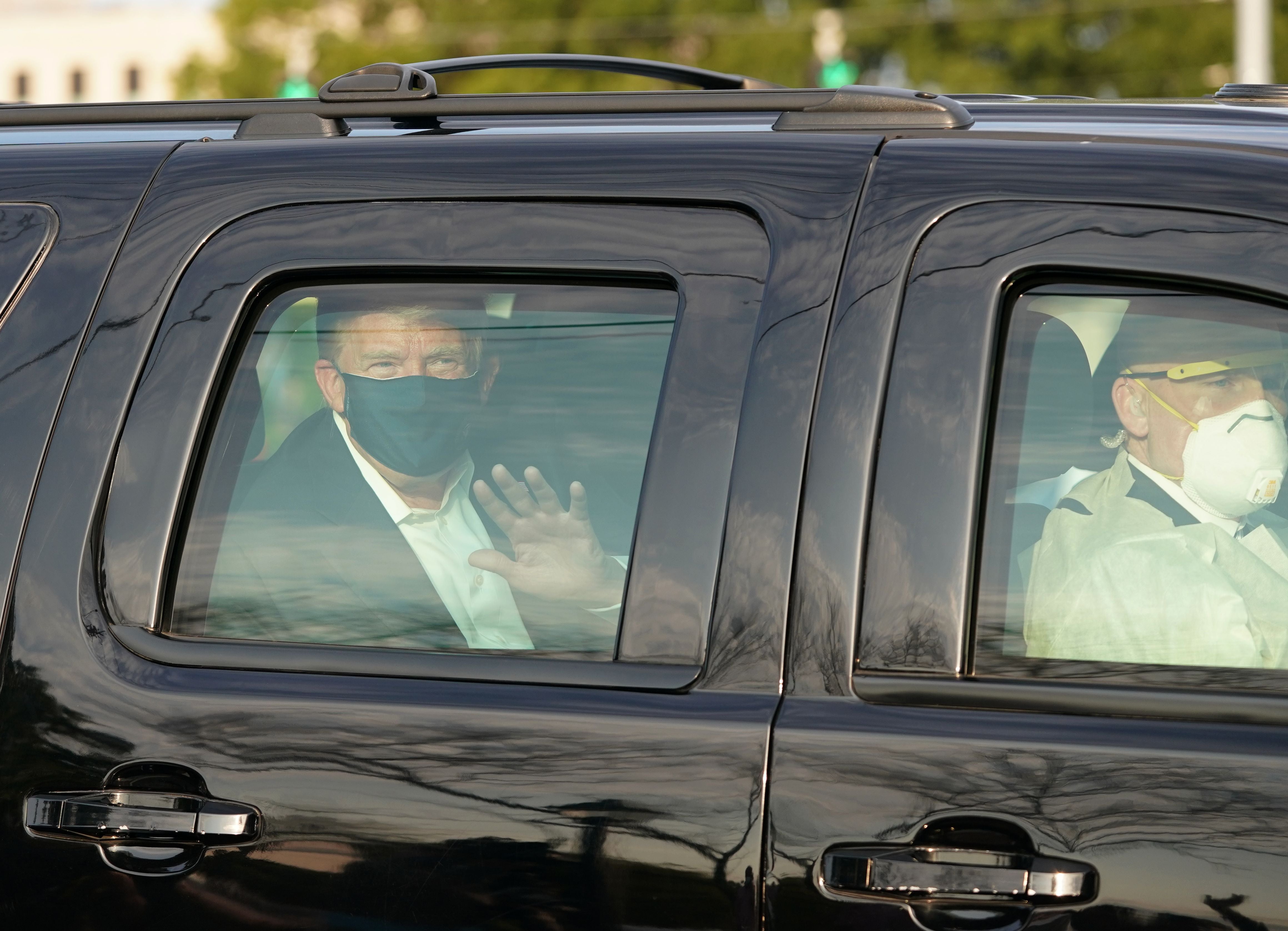 El presidente Trump saluda desde la parte trasera de un automóvil en una caravana fuera del Centro Médico Walter Reed en Bethesda, Maryland, el 4 de octubre de 2020.