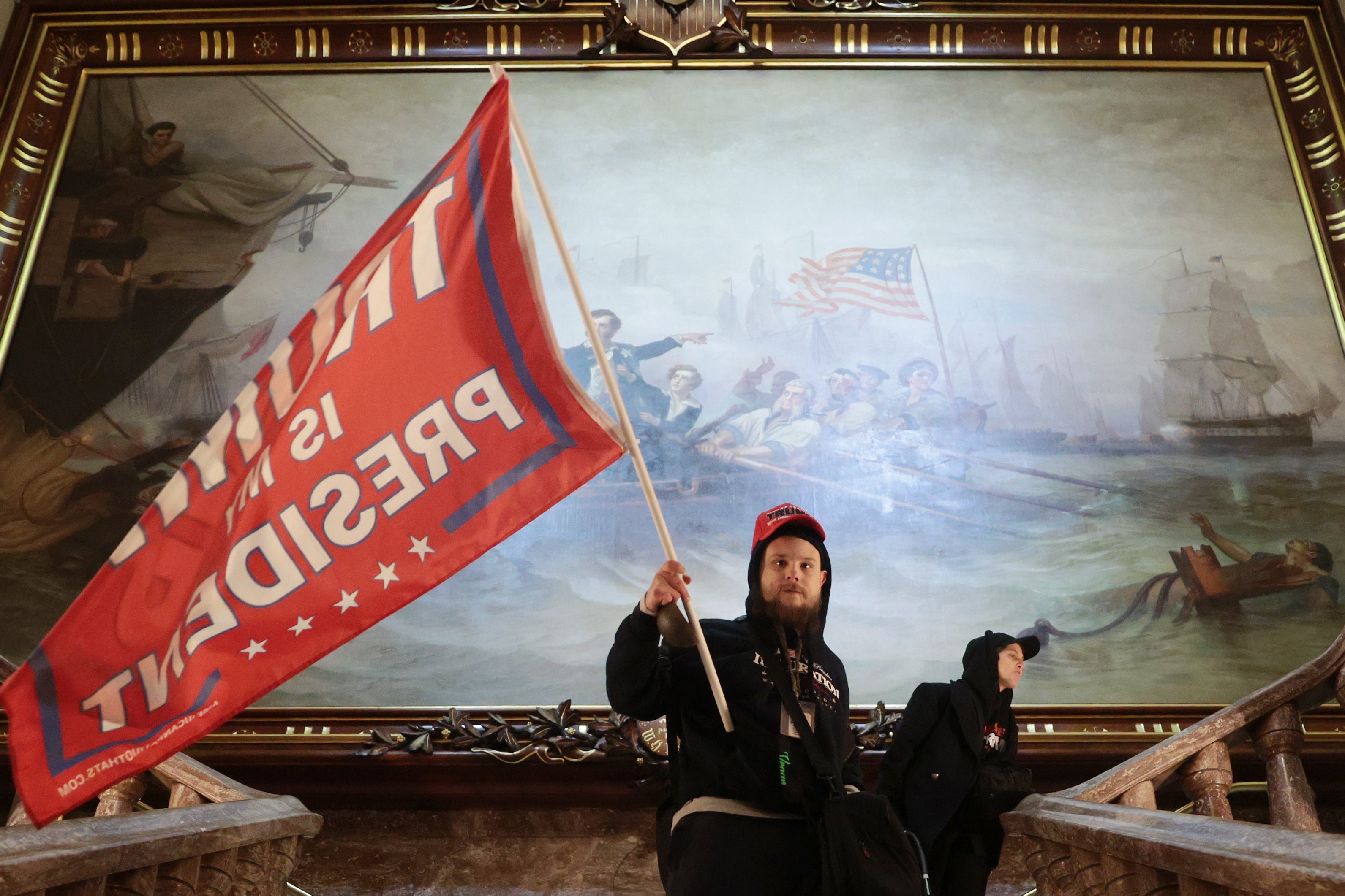 Un manifestante fue fotografiado ondeando una bandera de Trump frente a una enorme obra de arte del siglo XIX dentro del edificio del Capitolio.