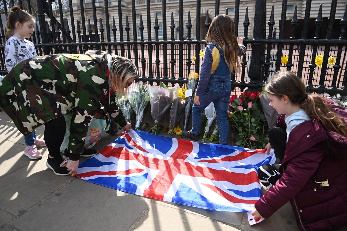 La gente coloca una bandera Union Jack junto a flores y mensajes de condolencia fuera del Palacio de Buckingham
