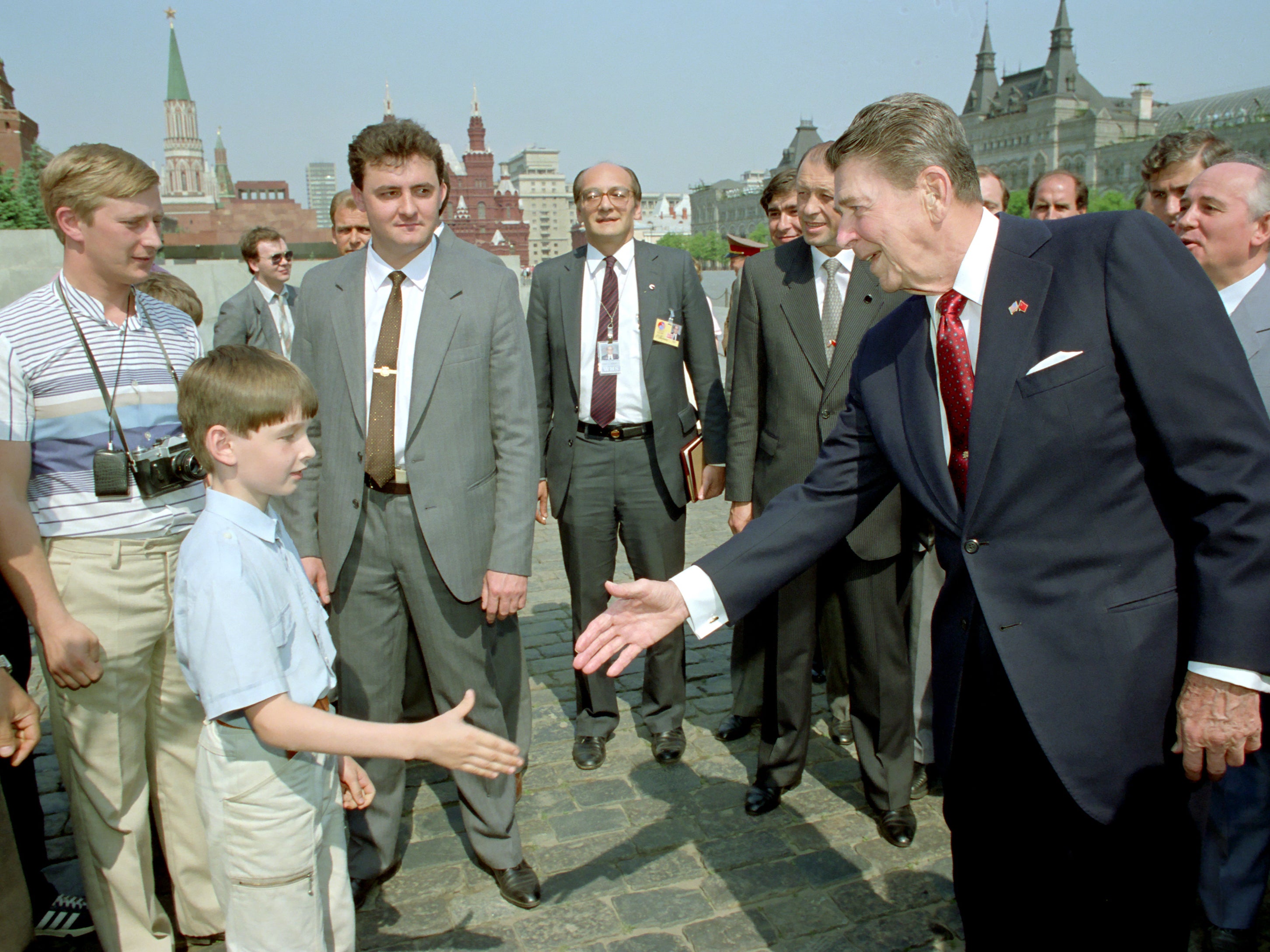 Ronald Reagan le da la mano a un niño mientras Mikhail Gorbachev (der.) observa durante un recorrido por la Plaza Roja de Moscú. ¿Podría también mostrar a un joven Vladimir Putin (izq.) espiando al presidente de Estados Unidos?