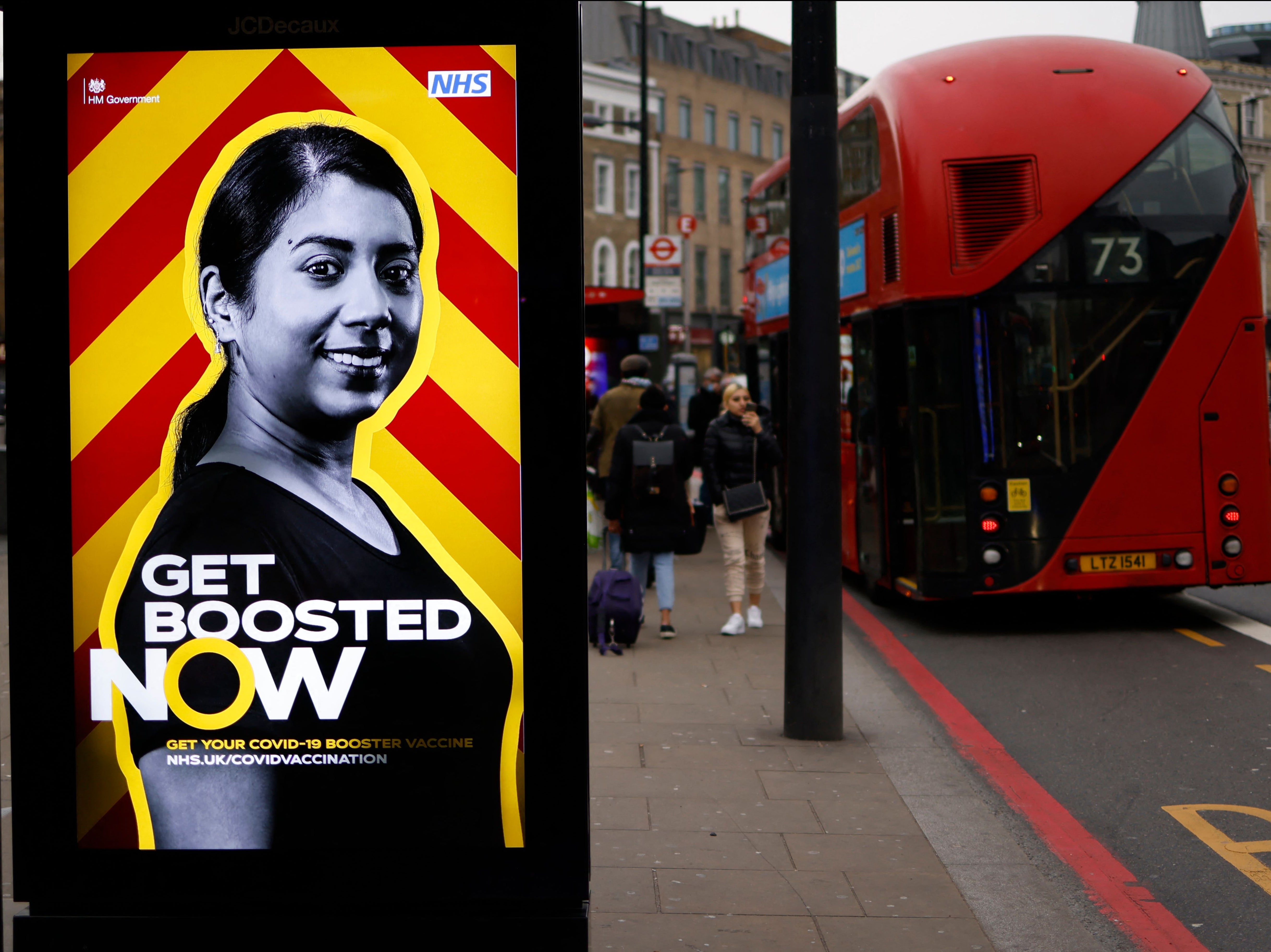 Un autobús londinense rojo se detiene en una parada de autobús que muestra un anuncio del gobierno que promueve el programa de vacunación covid-19 del NHS