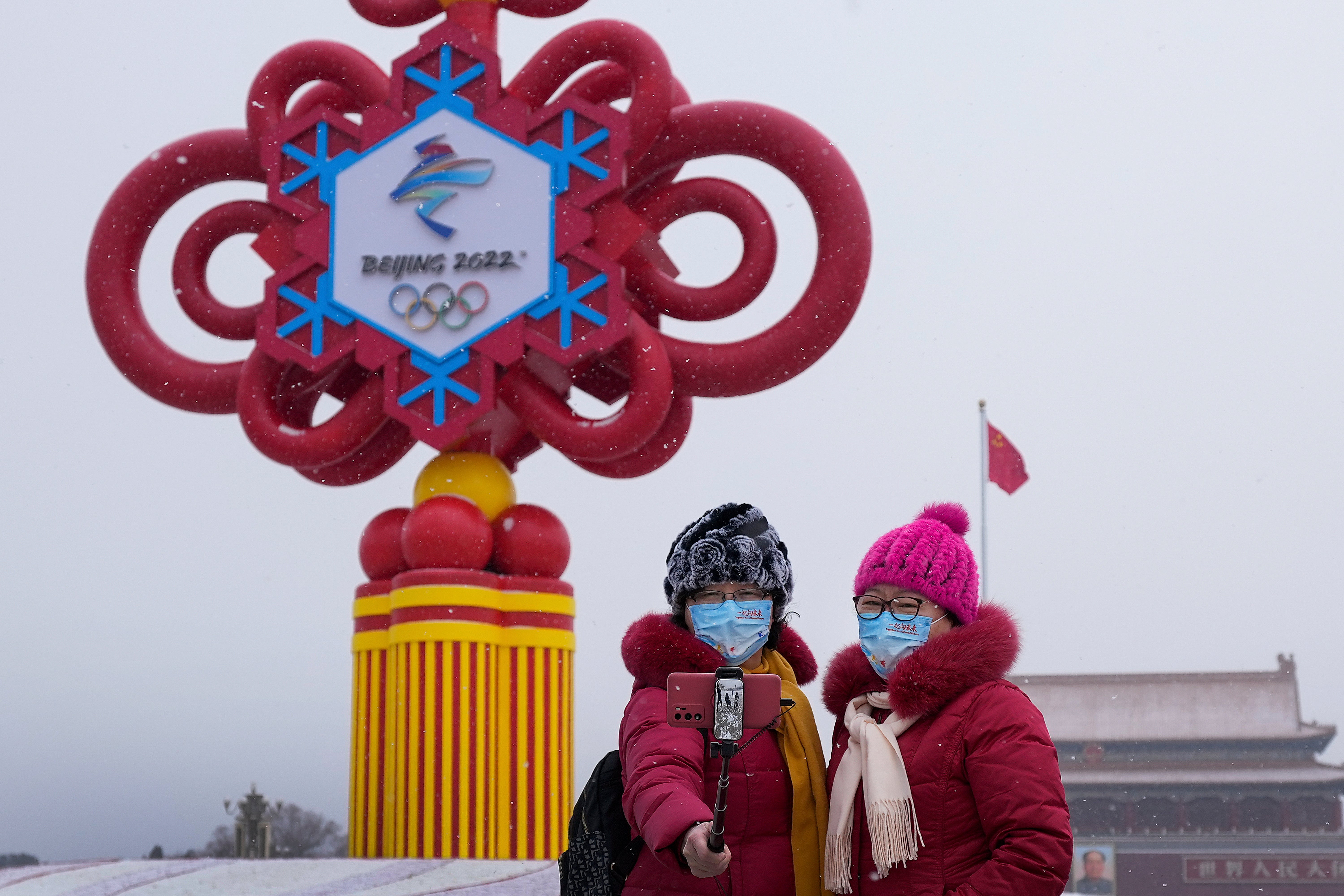 Mujeres con cubrebocas se toman una selfie con una decoración de los Juegos Olímpicos de Invierno en la Plaza de Tiananmen
