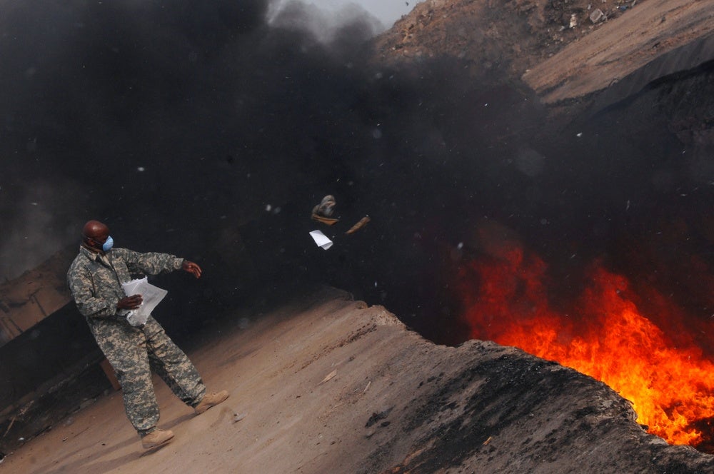 Un miembro del ejército de EE.UU. tira basura en un pozo de combustión