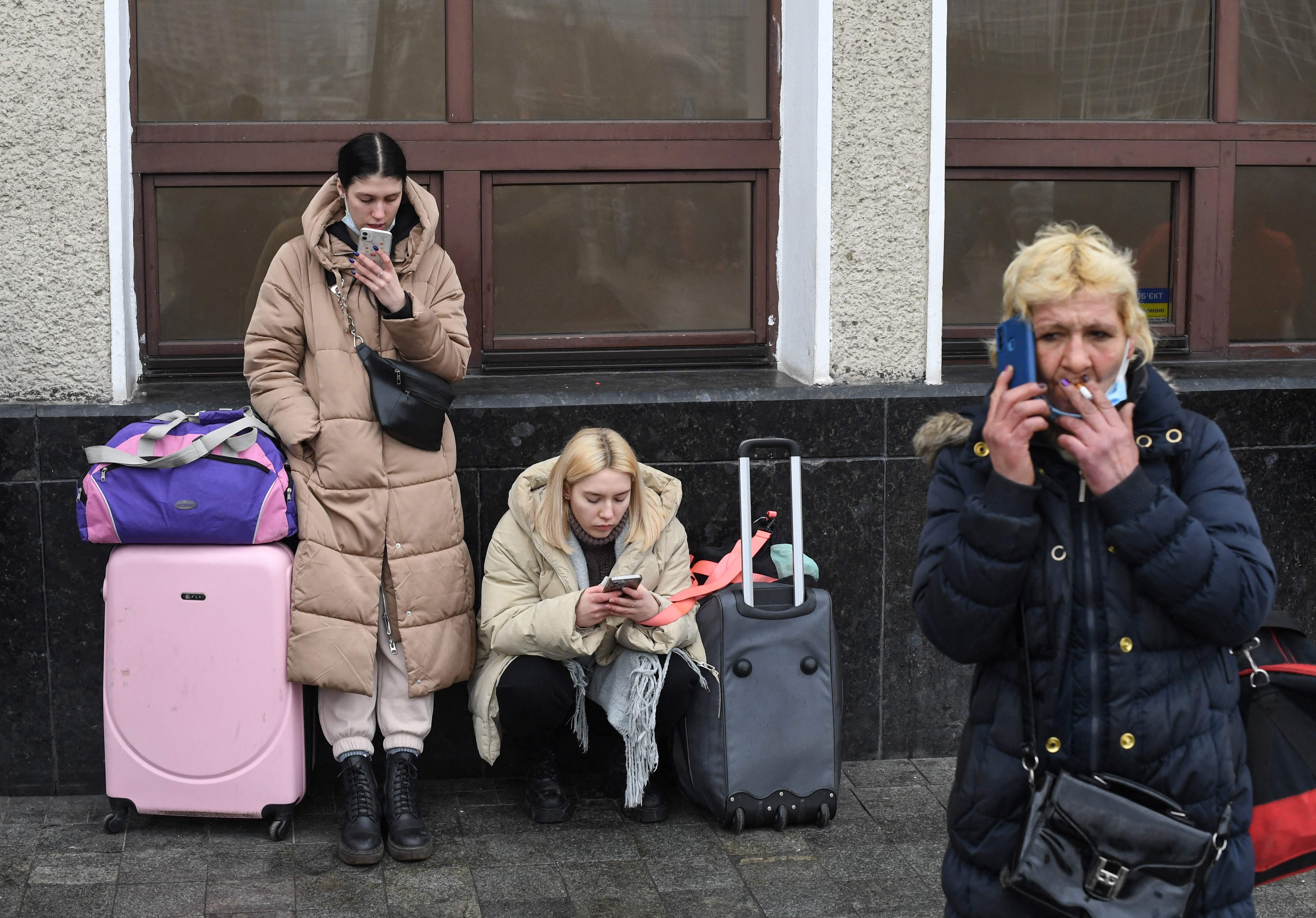 Mujeres usan su teléfono mientras esperan con bolsas y maletas cerca de la estación de tren de Kiev-Pasazhyrskyi