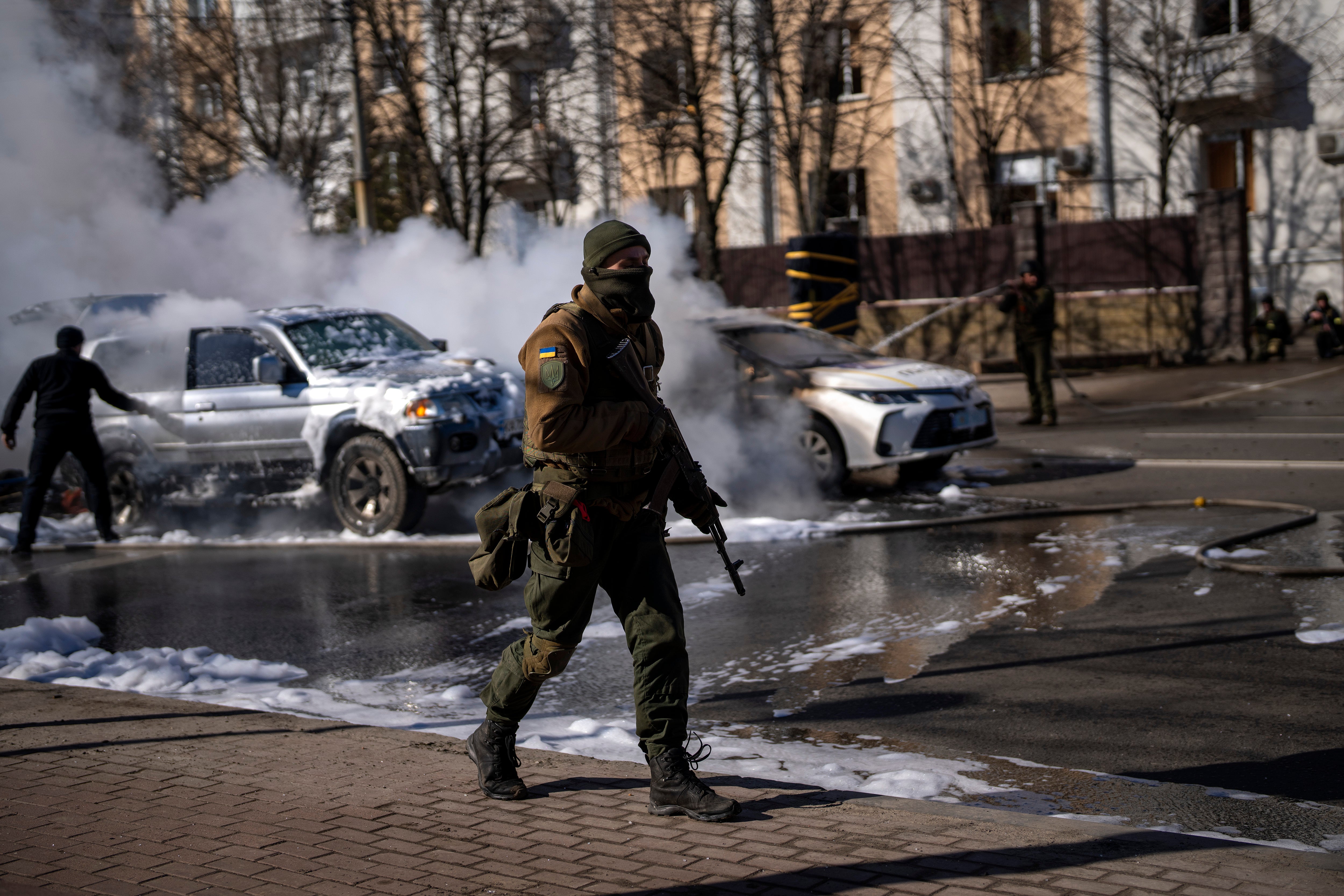 Los soldados ucranianos toman sus posiciones fuera de una base militar mientras se incendian dos coches en una calle de Kiev el sábado