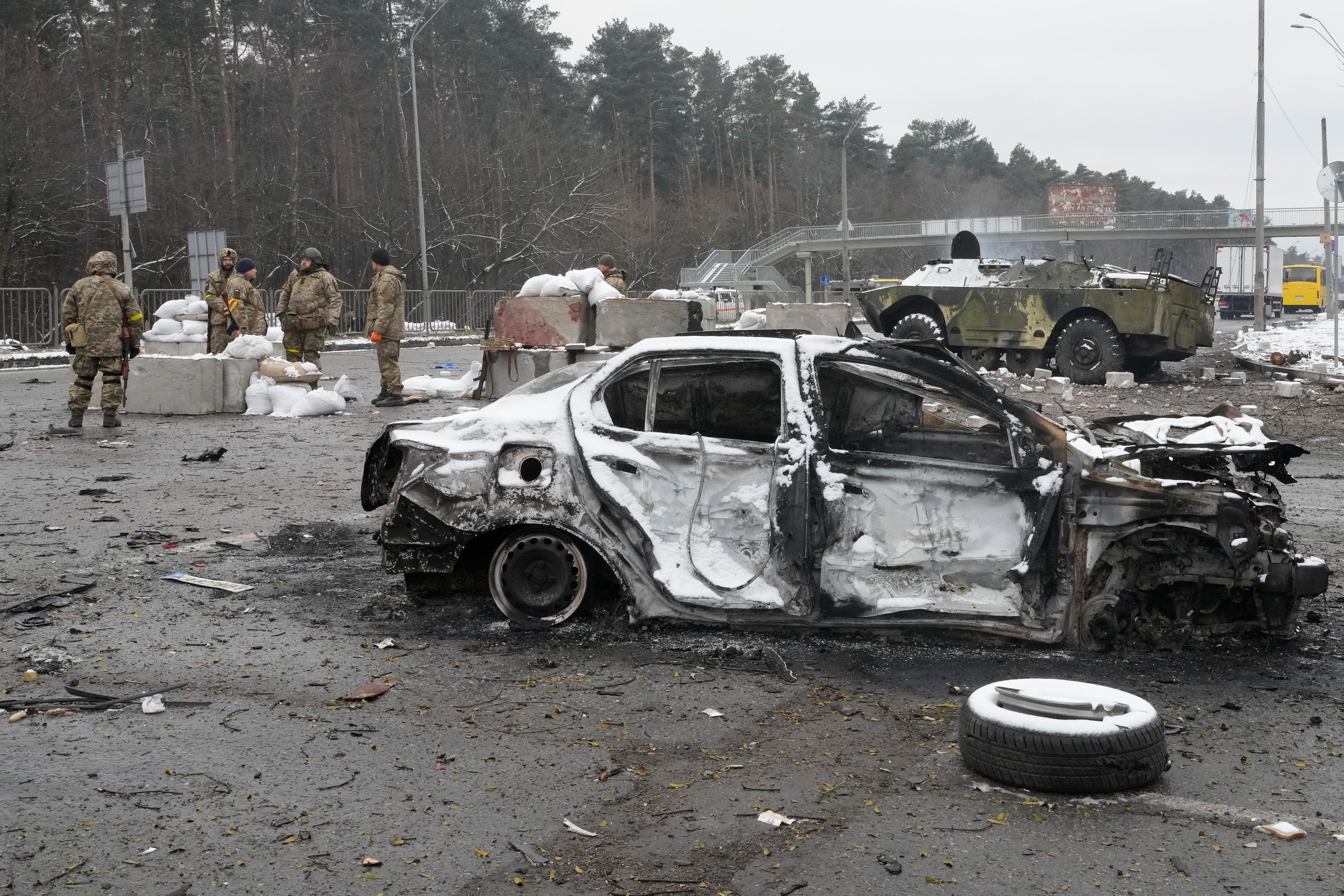 Militares ucranianos se paran cerca de un automóvil dañado y un vehículo blindado en un puesto de control en las afueras de Kyiv