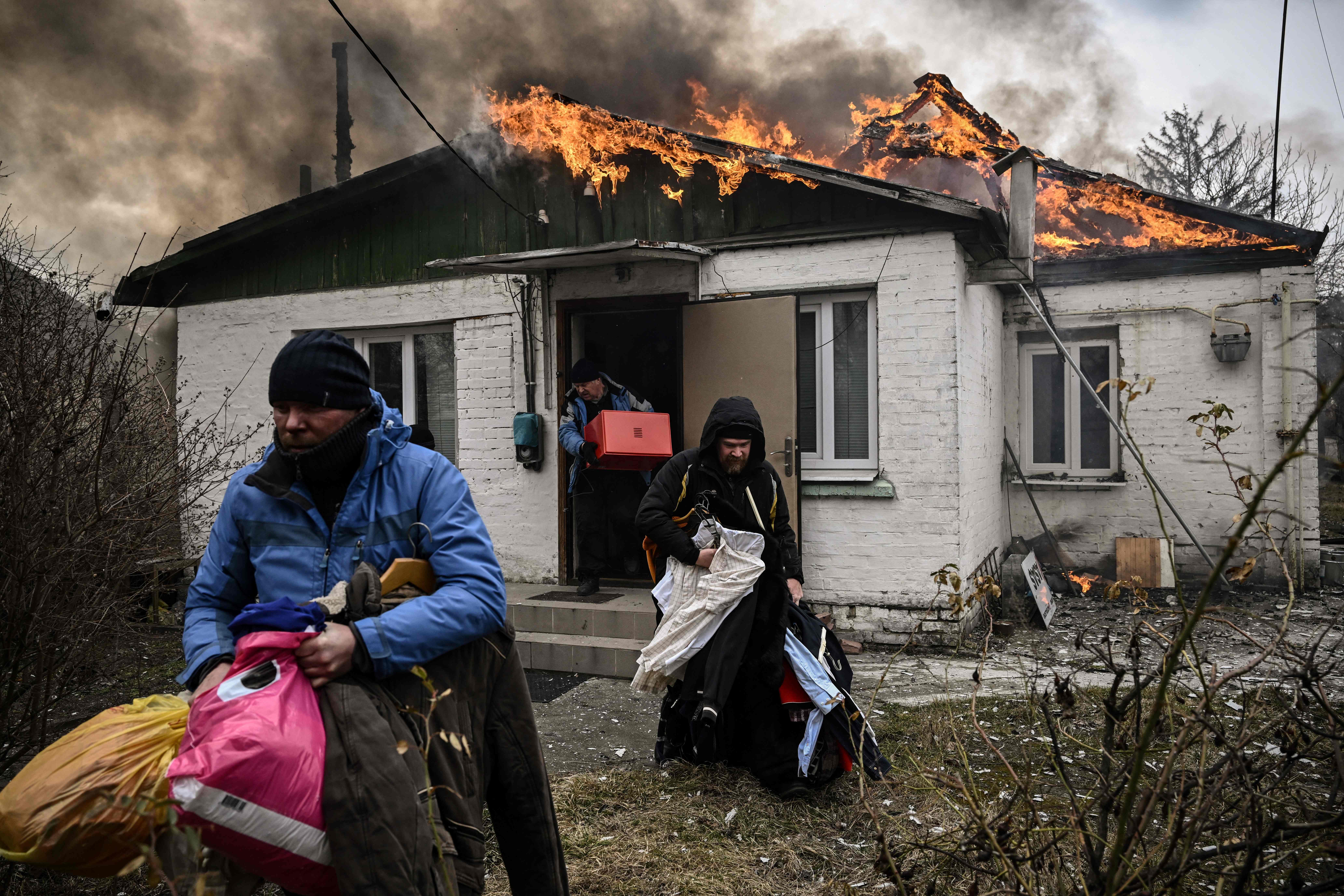 Personas sacan sus pertenencias de una casa en llamas luego de un bombardeo en la ciudad de Irpin, en las afueras de Kyiv