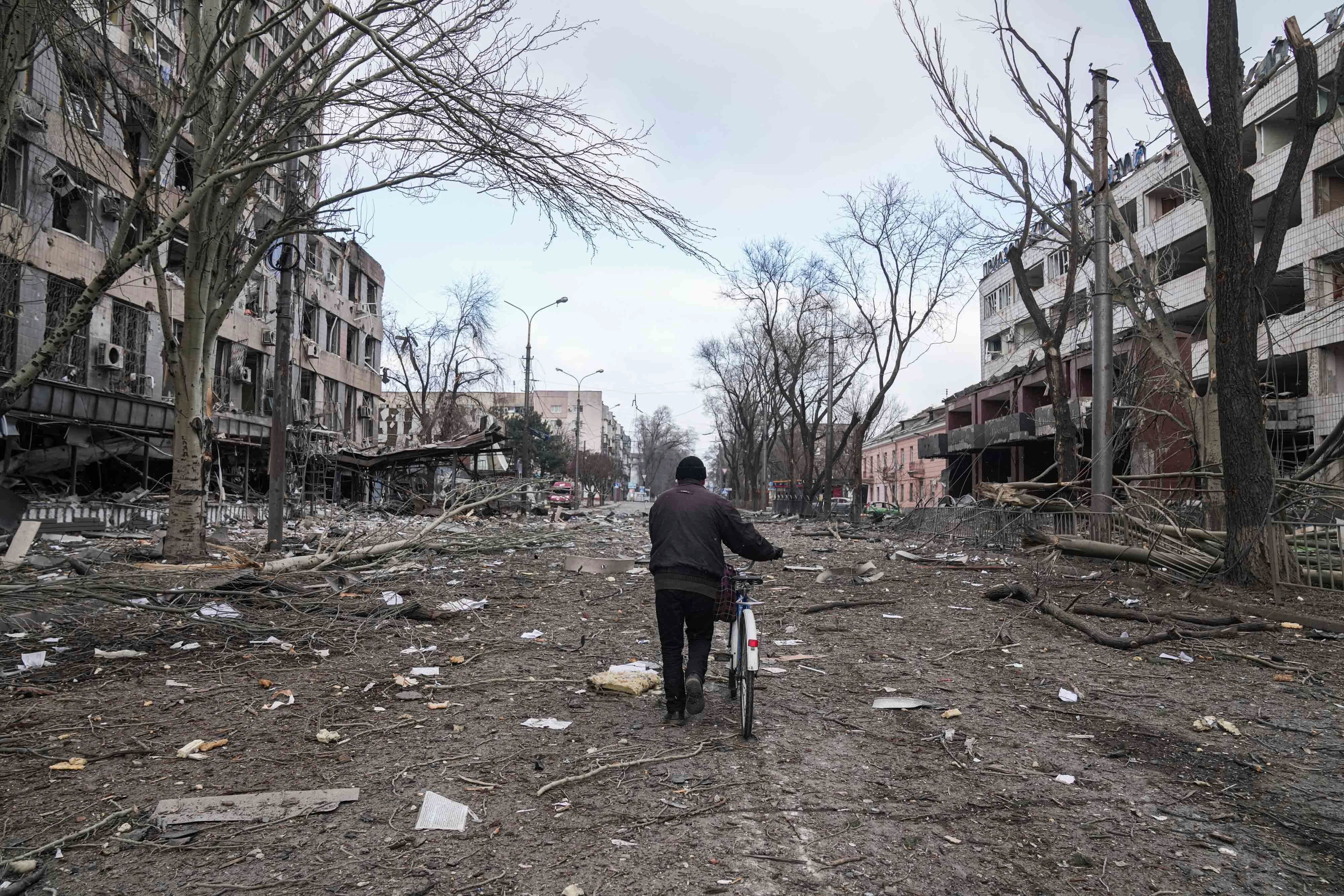 Un hombre camina con una bicicleta en una calle dañada por los bombardeos en Mariúpol, Ucrania, el jueves 10 de marzo de 2022