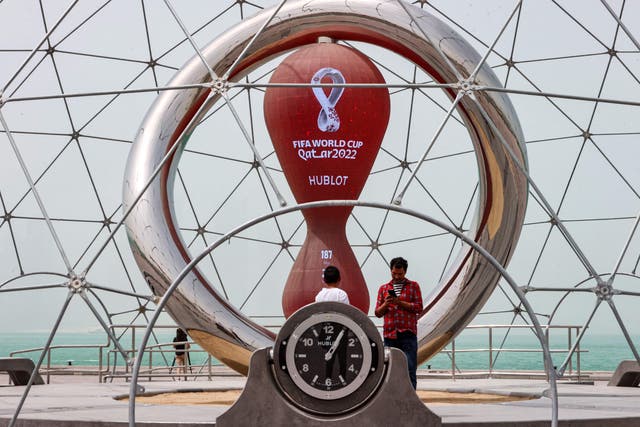 <p>People stand by the clock installation ticking the days to the start of the Qatar 2022 FIFA World Cup, along the waterfront in Qatar's capital Doha</p>