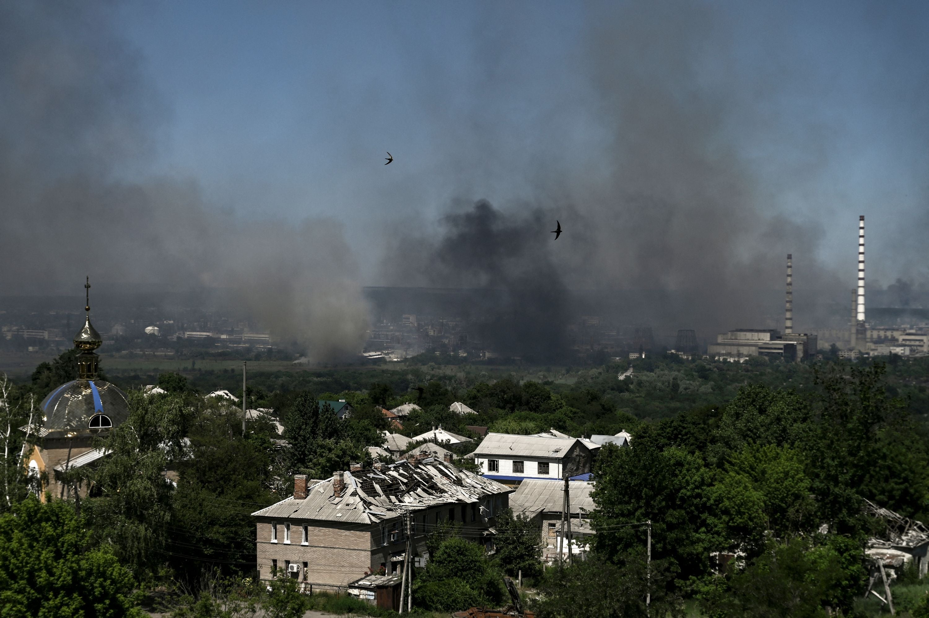 Black smoke and dirt rise from Severodonetsk during a battle between Russian and Ukrainian troops, while a damaged building is pictured in nearby Lysychansk