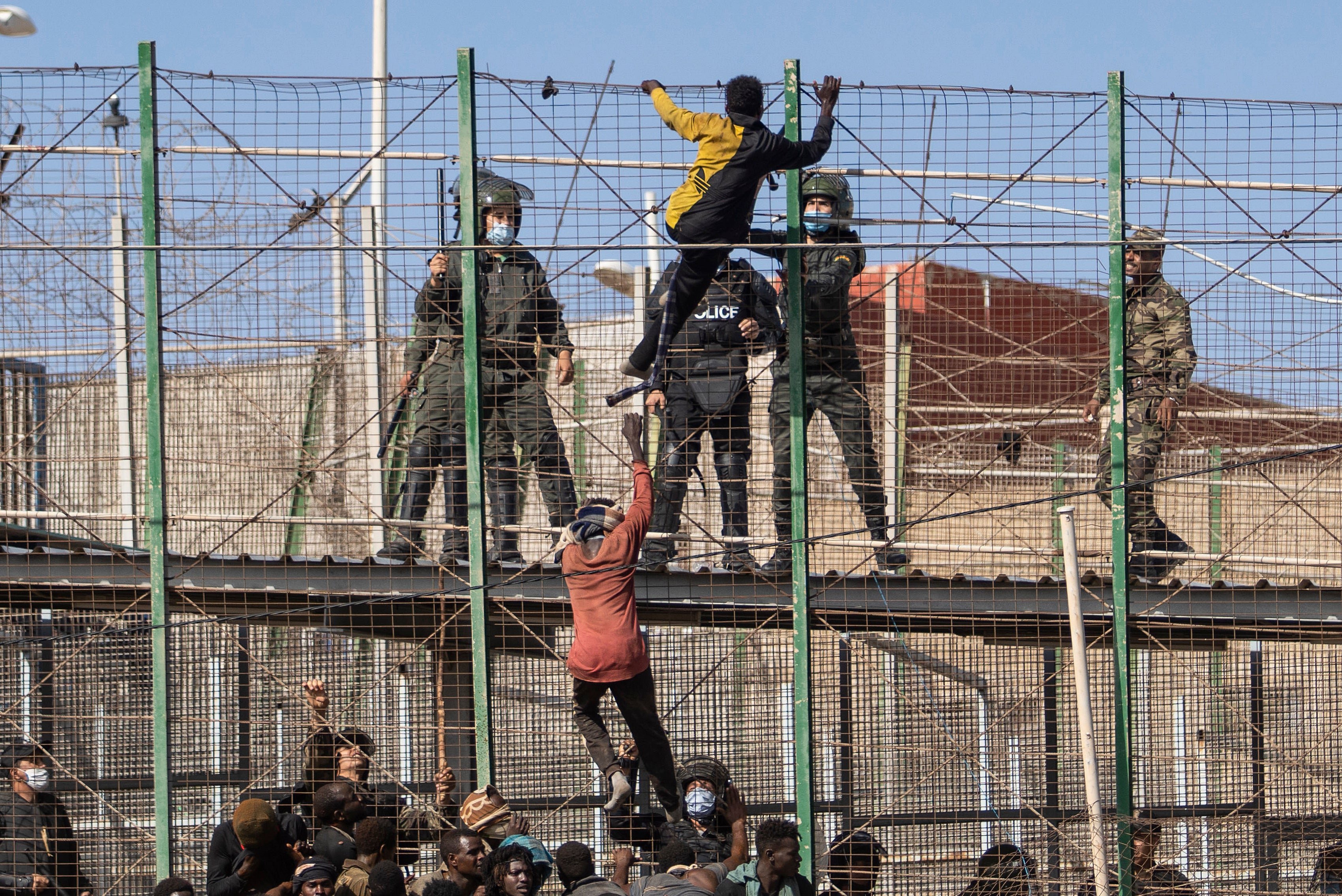 Personas escalan las vallas que separan el enclave español de Melilla de Marruecos el viernes
