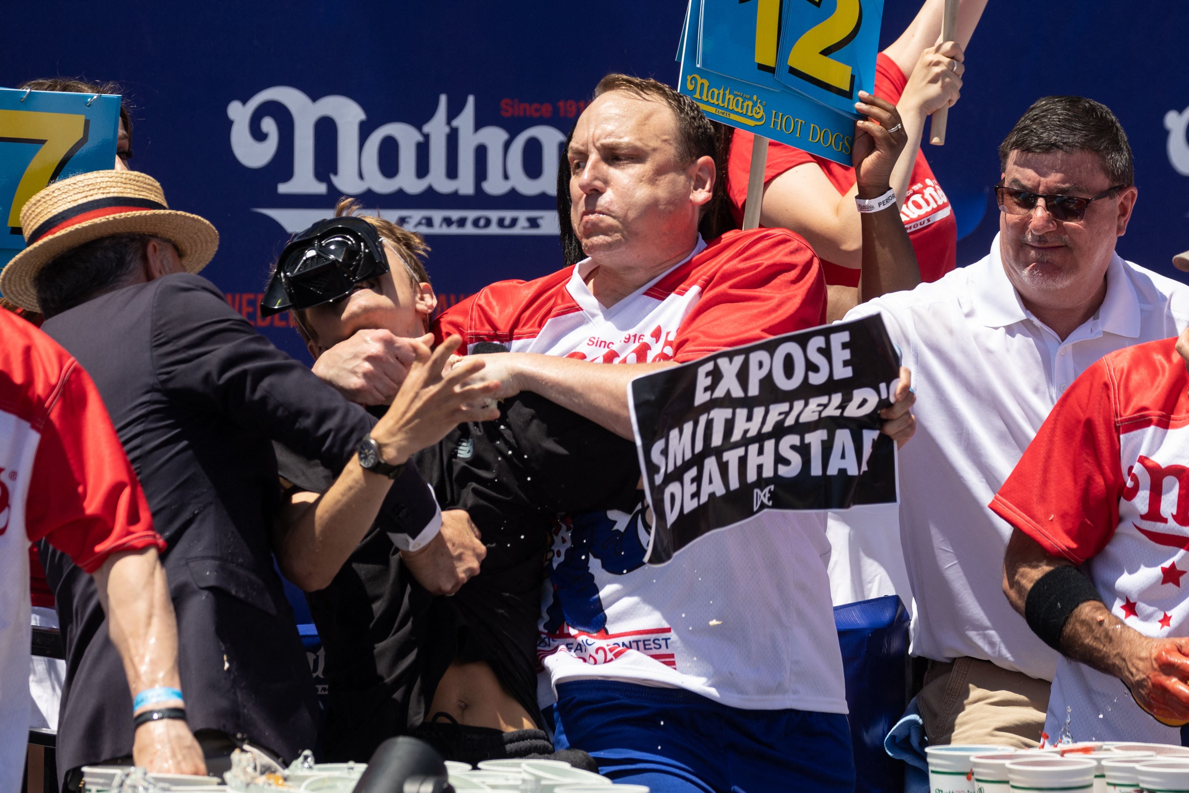 Joey Chestnut derriba a un manifestante que interrumpió la competición durante el Concurso Internacional de Hot Dogs de Nathan’s Famous del 4 de julio en Coney Island en Nueva York