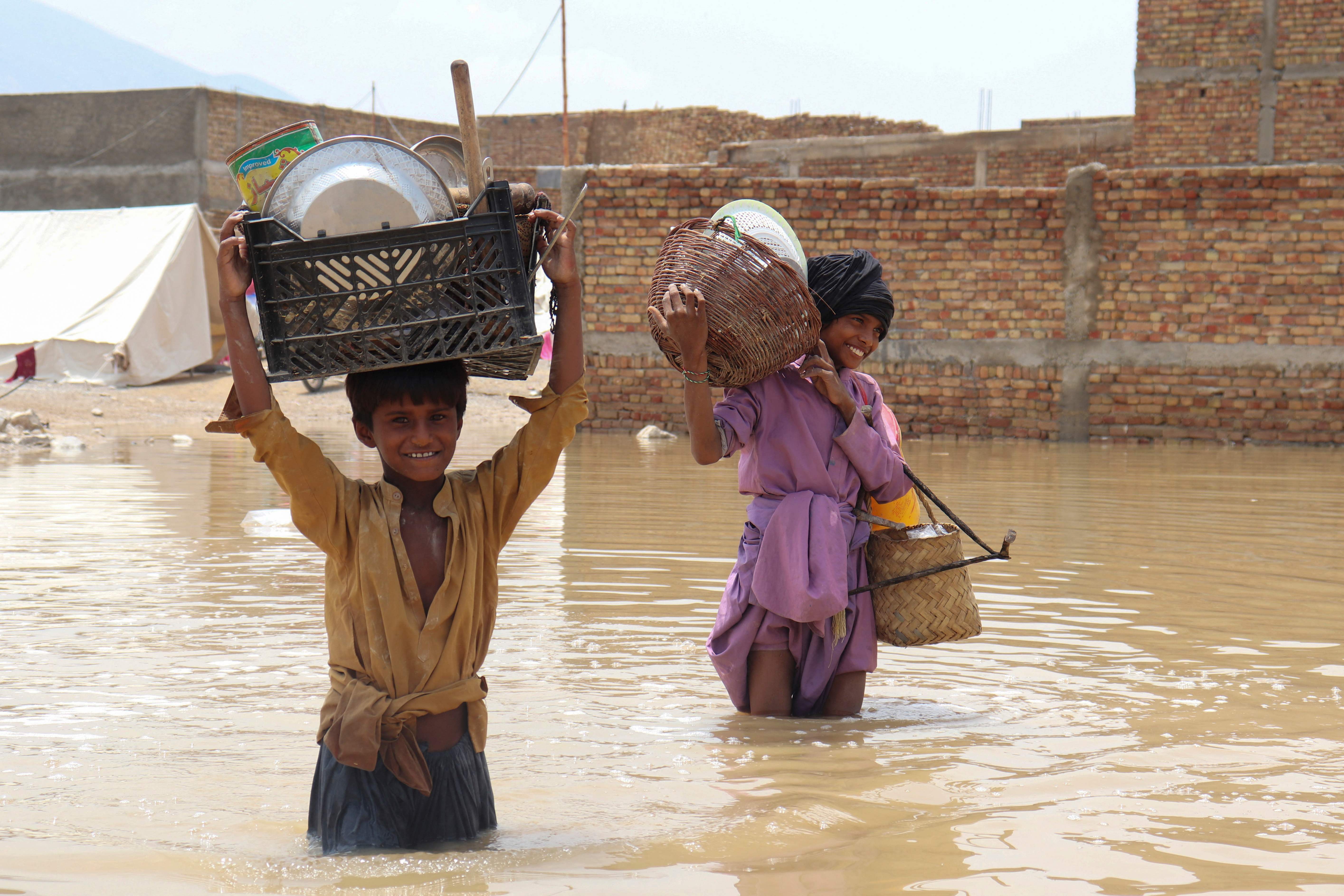 Niños cargan artículos domésticos mientras atraviesan un área inundada después de una lluvia monzónica en Quetta