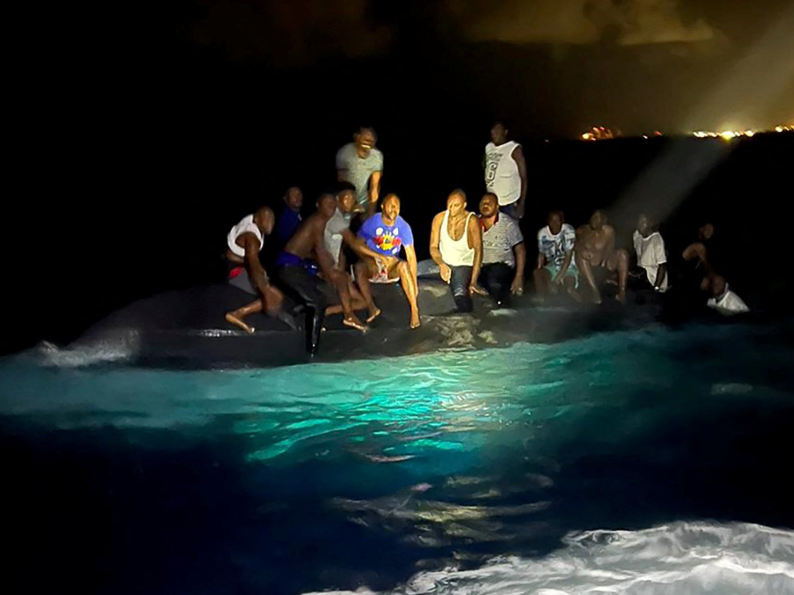 Los sobrevivientes de un bote con migrantes que volcó se posan sobre la embarcación volcada frente a la costa de la isla de Nueva Providencia