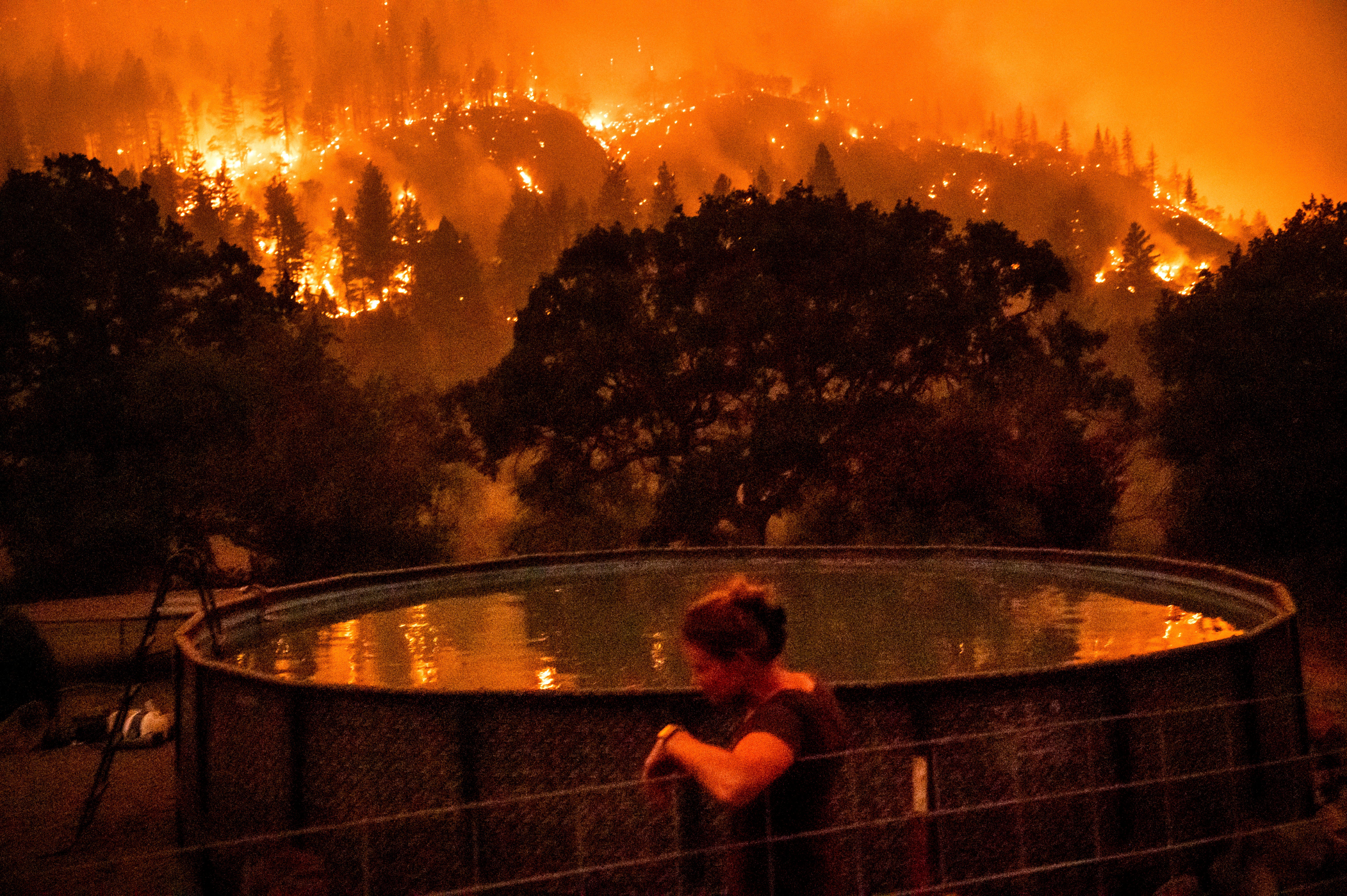Angela Crawford se recarga contra una cerca mientras el incendio McKinney quema la ladera de una colina sobre su casa en el Bosque Nacional Klamath, en California, el sábado 30 de julio de 2022