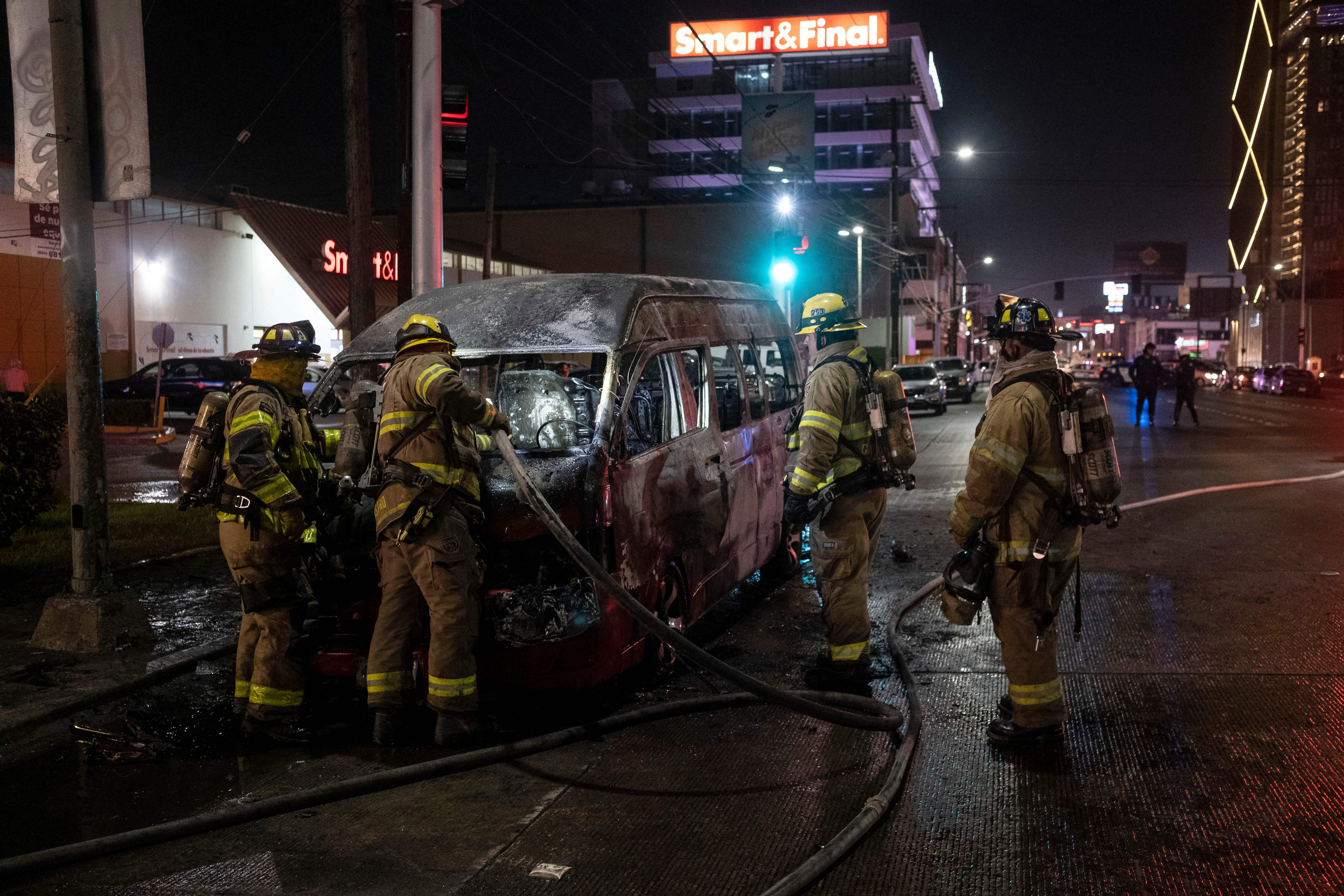 Los bomberos trabajan en la escena de un vehículo de transporte colectivo quemado después de que fuera incendiado por individuos no identificados en Tijuana, estado de Baja California, México, el 12 de agosto de 2022