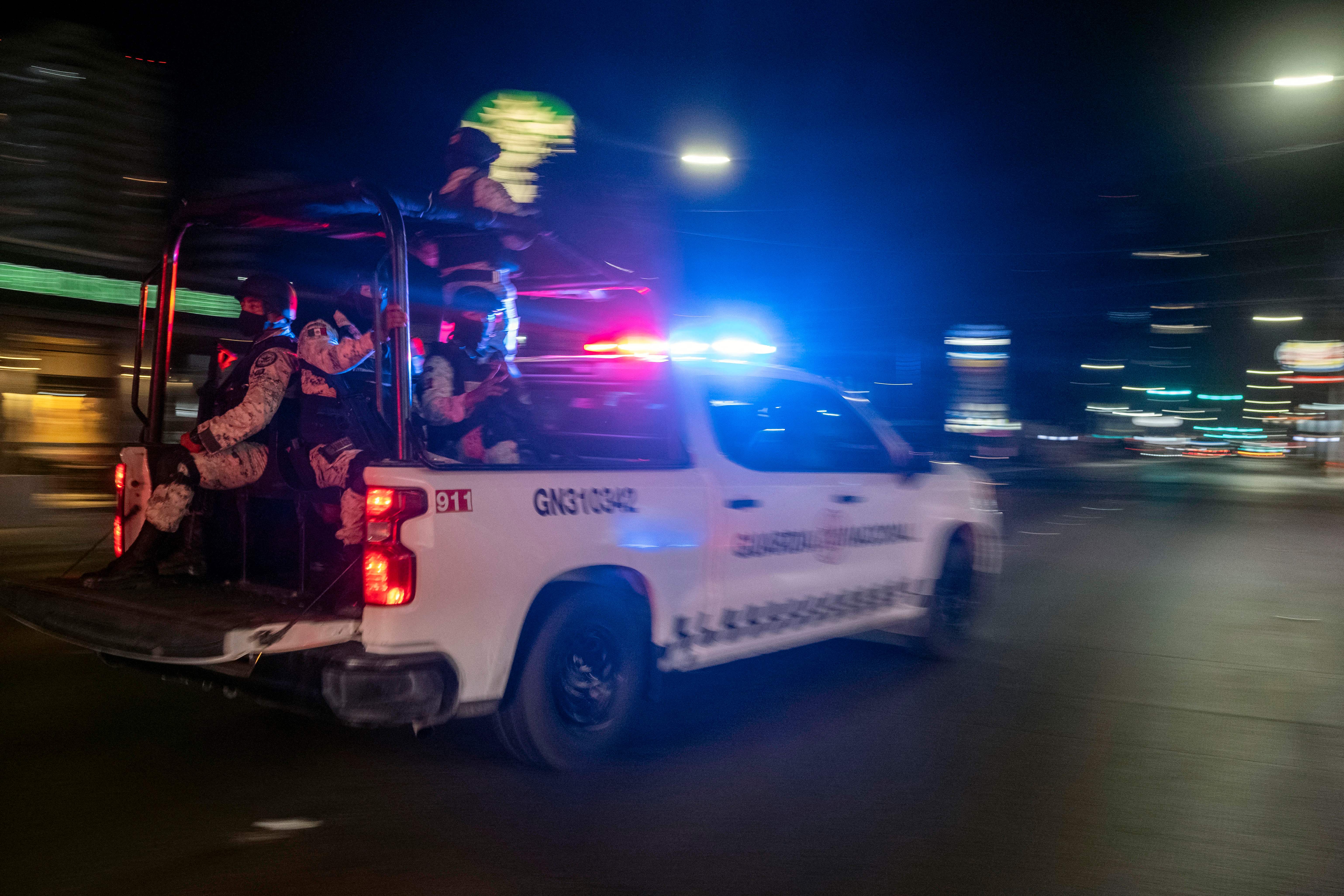 Miembros armados de la Guardia Nacional pasan por delante del lugar donde se encuentra un vehículo de transporte colectivo quemado tras ser incendiado por individuos no identificados en Tijuana, estado de Baja California, México, el 12 de agosto de 2022