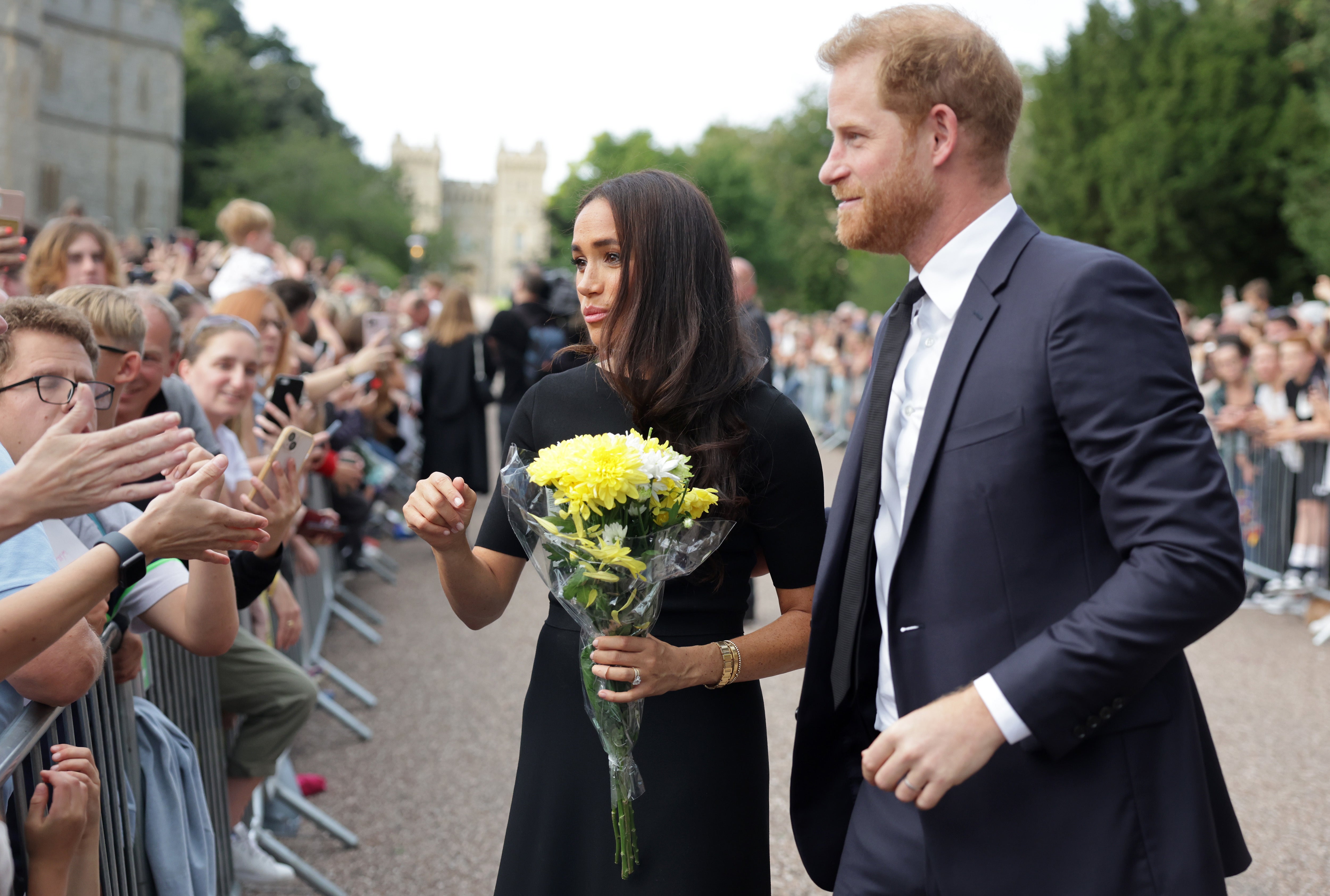 Harry y Meghan se encuentran con personas del público mientras observan las flores dejadas como tributo en el Castillo de Windsor el sábado