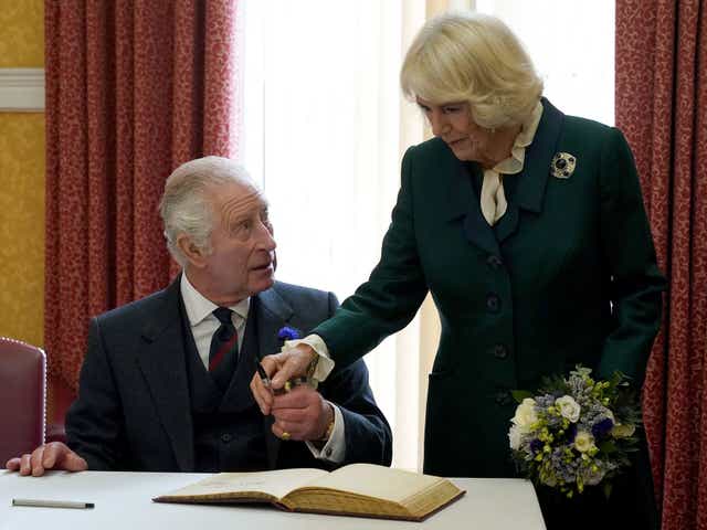 El rey Carlos III (L) y la británica Camilla, la reina consorte sostienen un bolígrafo mientras firman un libro de visitantes después de asistir a una reunión oficial del consejo en las Cámaras de la ciudad de Dunfermline.