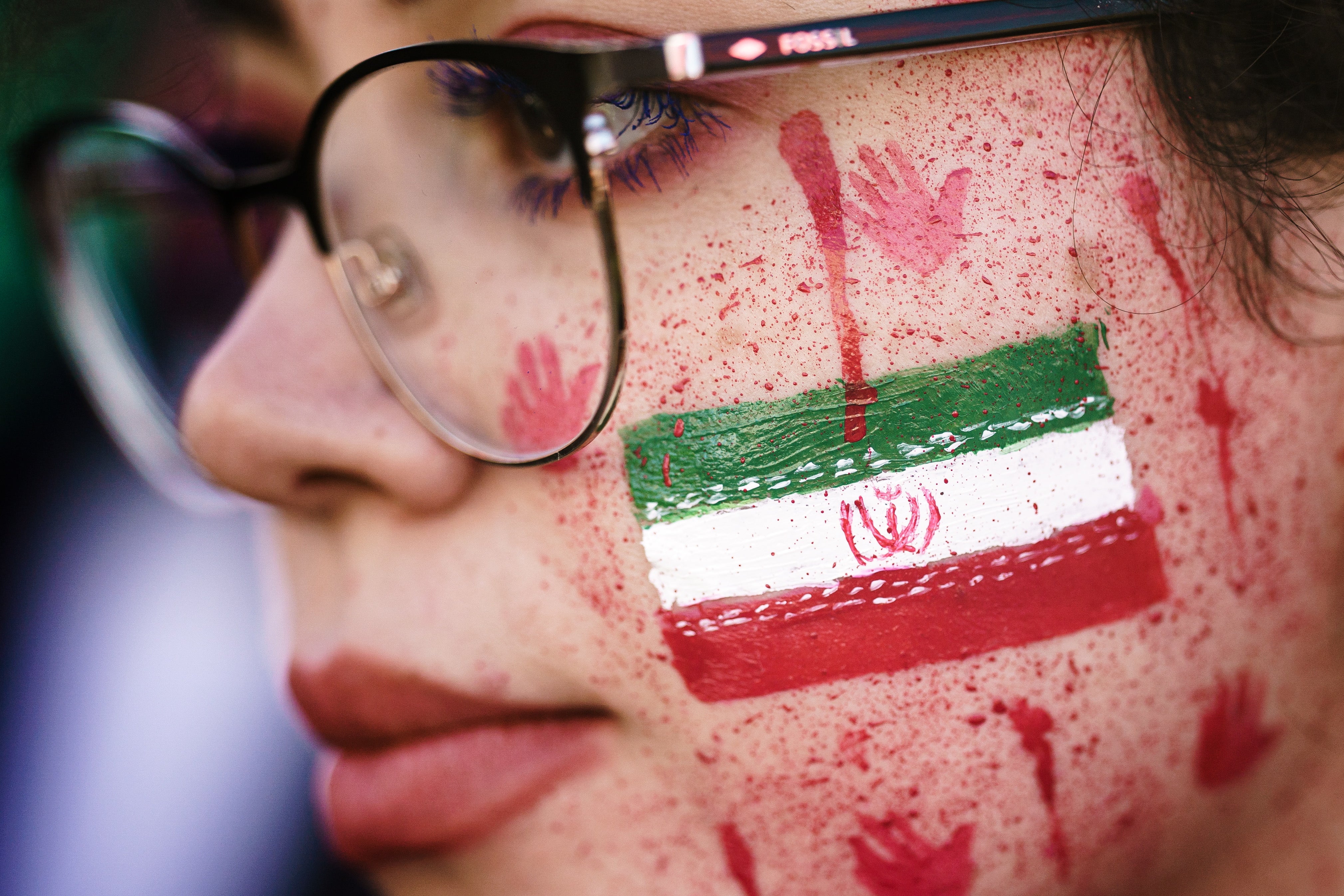 Una manifestante muestra pintura roja en su cara que asemeja salpicaduras de sangre y huellas de manos ensangrentadas junto al emblema nacional iraní