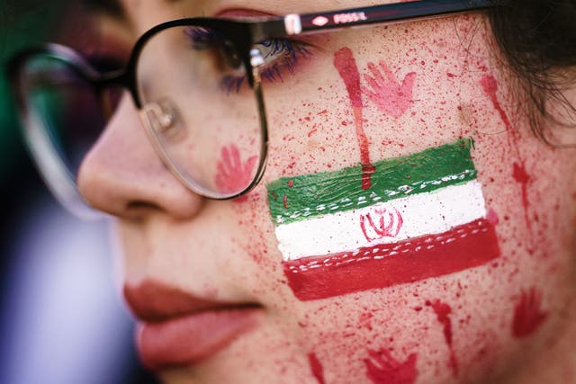 Una manifestante muestra pintura roja en su rostro, que se asemeja a salpicaduras de sangre y huellas de manos ensangrentadas junto al emblema nacional iraní.