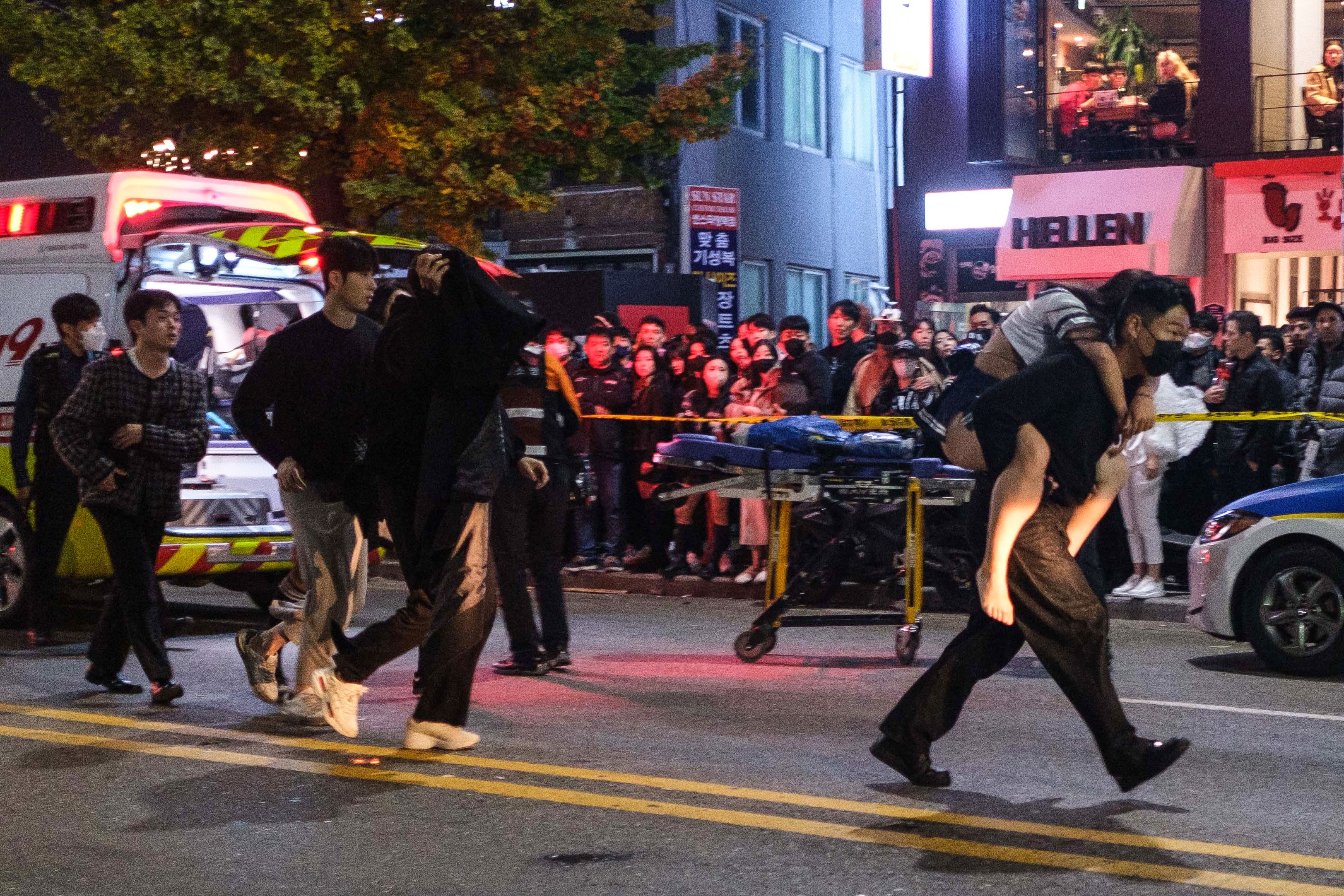 Un hombre carga a una mujer, que resultó herida en una estampida durante la celebración de Halloween, hacia una ambulancia
