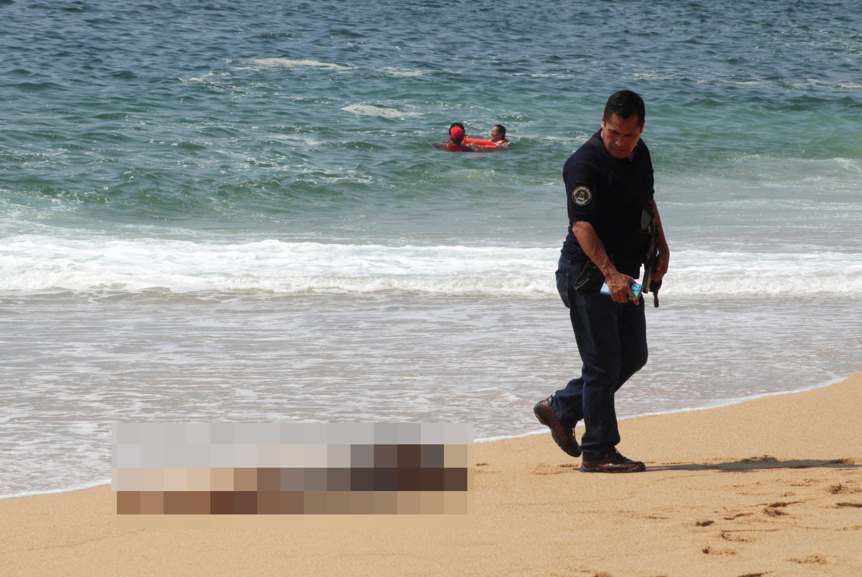 MATERIAL SENSIBLE. ESTA IMAGEN PUEDE OFENDER O MOLESTAR. Un policía camina cerca de uno de los tres cadáveres con signos de tortura que fueron arrastrados por el mar, según medios locales, en la playa de Icacos, en Acapulco