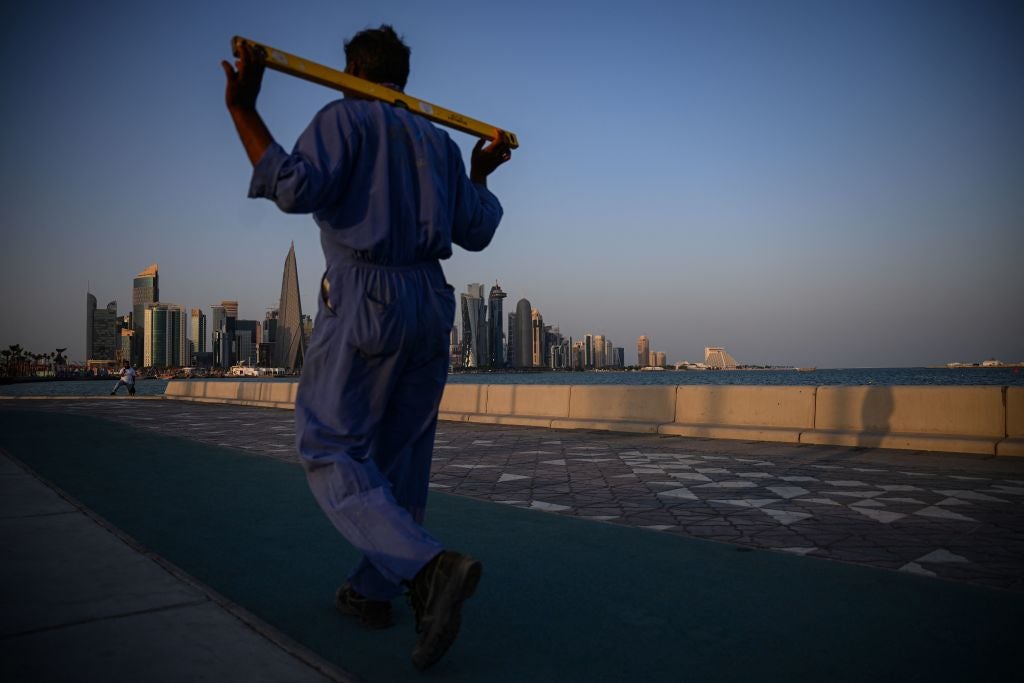 Un trabajador camina por la Corniche de Doha con el West Bay en el fondo