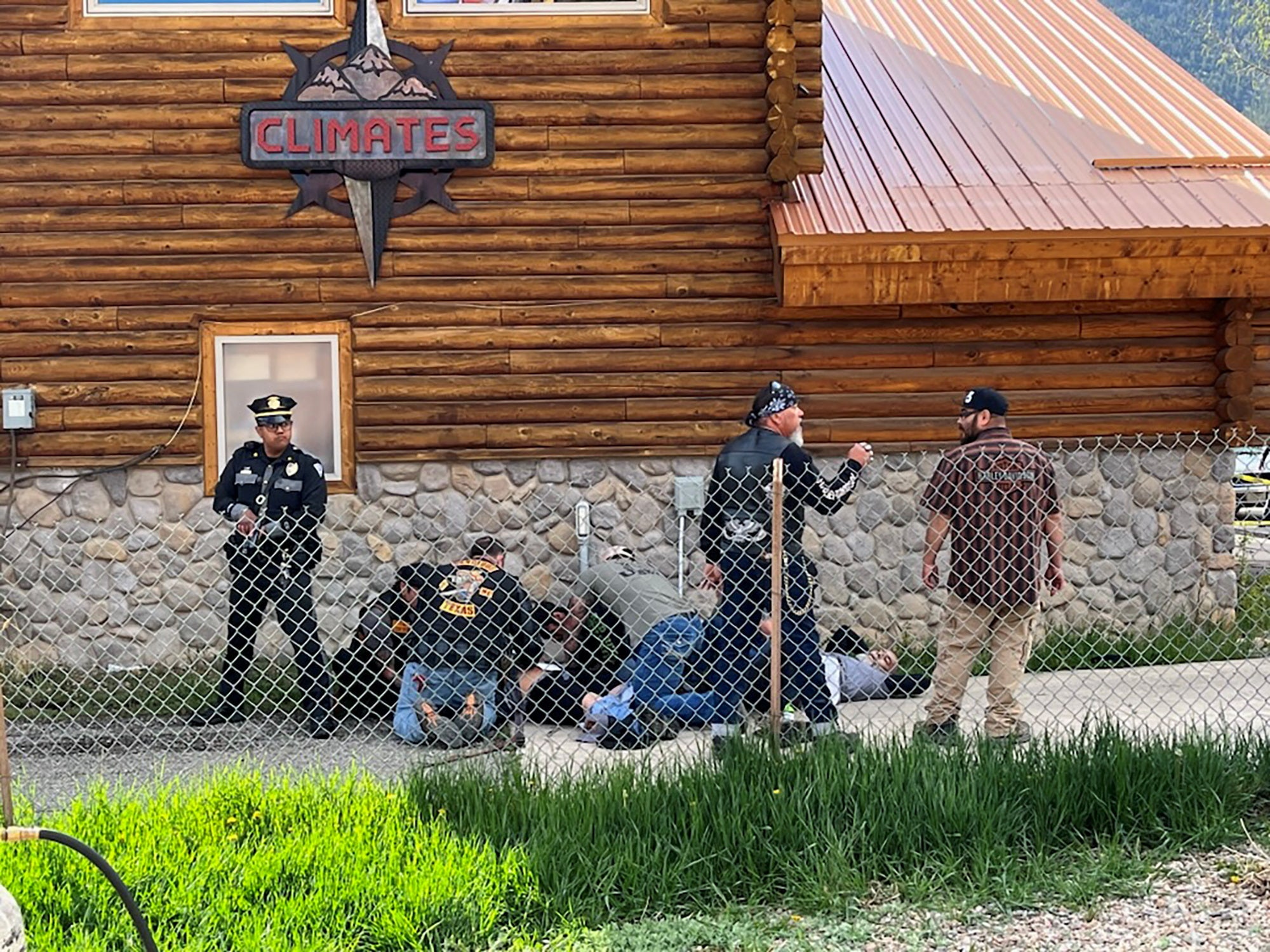 Un agente de policía monta guardia mientras un hombre con un parche de Bandidos MC brinda asistencia a un motociclista herido en Red River, Nuevo México, tras un tiroteo entre miembros de dos bandas de motociclistas en el rally anual de motos del Día de los Caídos