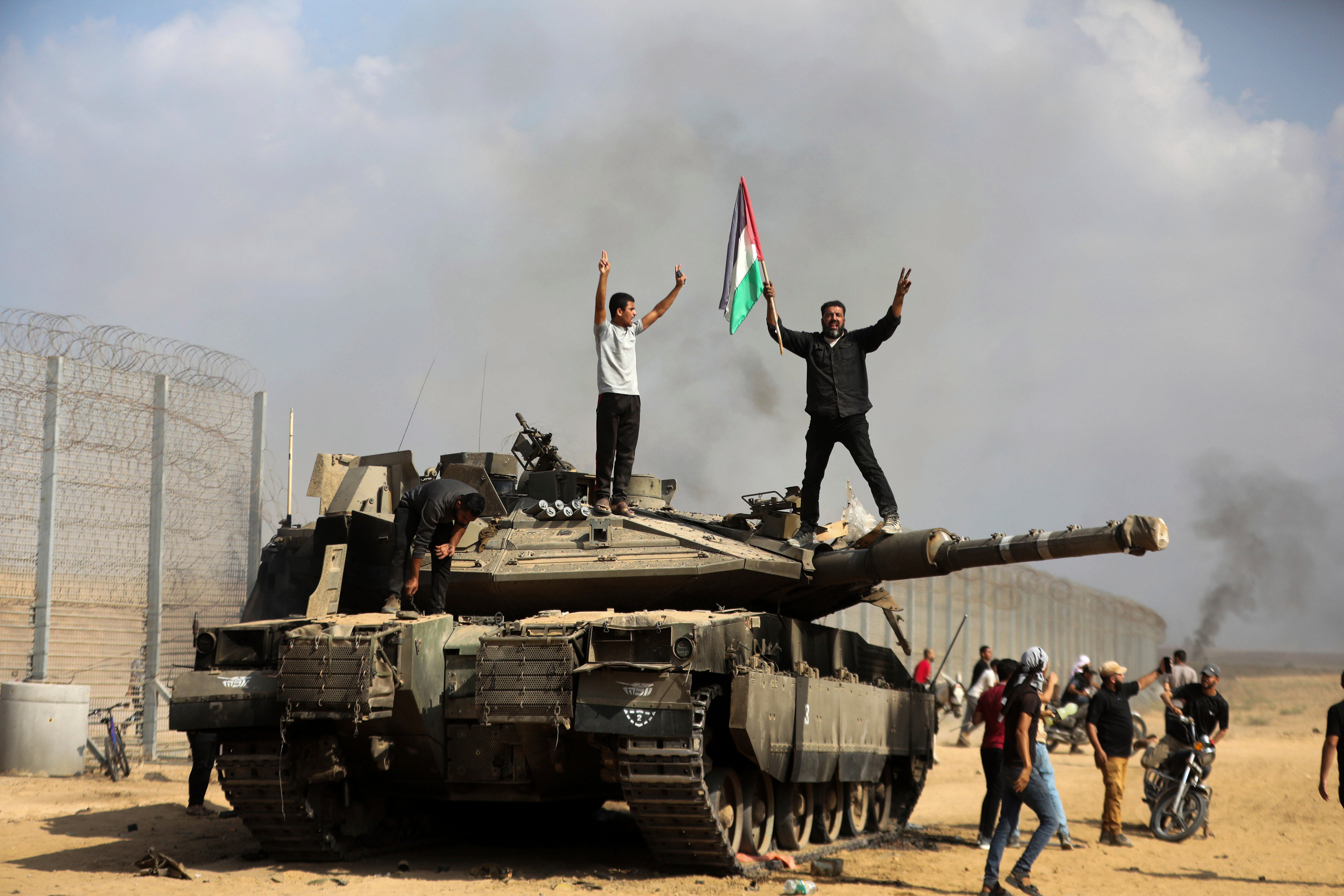 Palestinos agitan su bandera nacional y celebran junto a un tanque israelí destruido en el sur de la barda de la Franja de Gaza