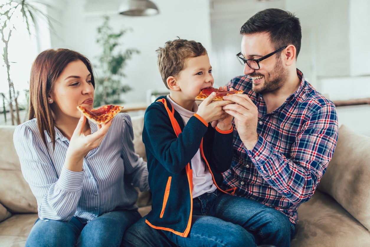 Familia feliz comiendo pizza sentada en el sofá de casa