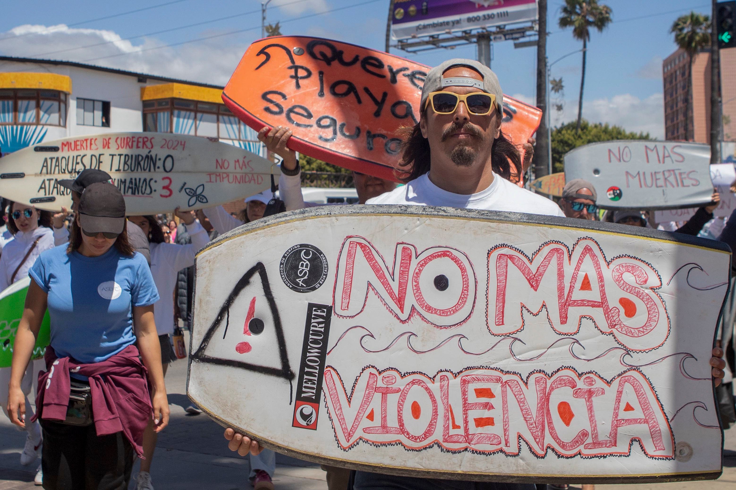 Un manifestante sostiene un bodyboard con la inscripción en español “No más violencia”