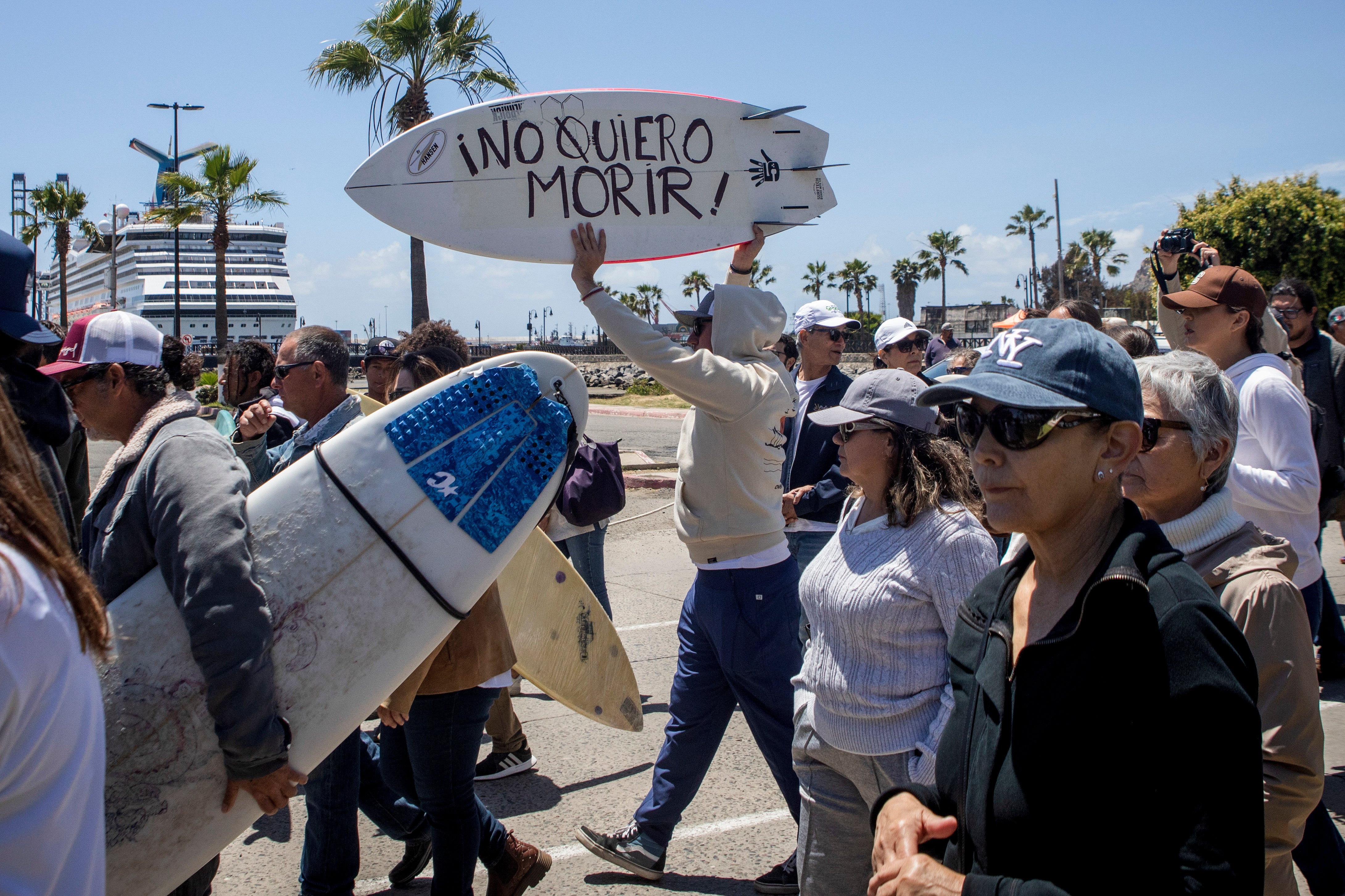 Un manifestante sostiene una tabla de bodyboard con la leyenda “¡No quiero morir!” mientras protesta por los asesinatos de surfistas extranjeros en Ensenada, México
