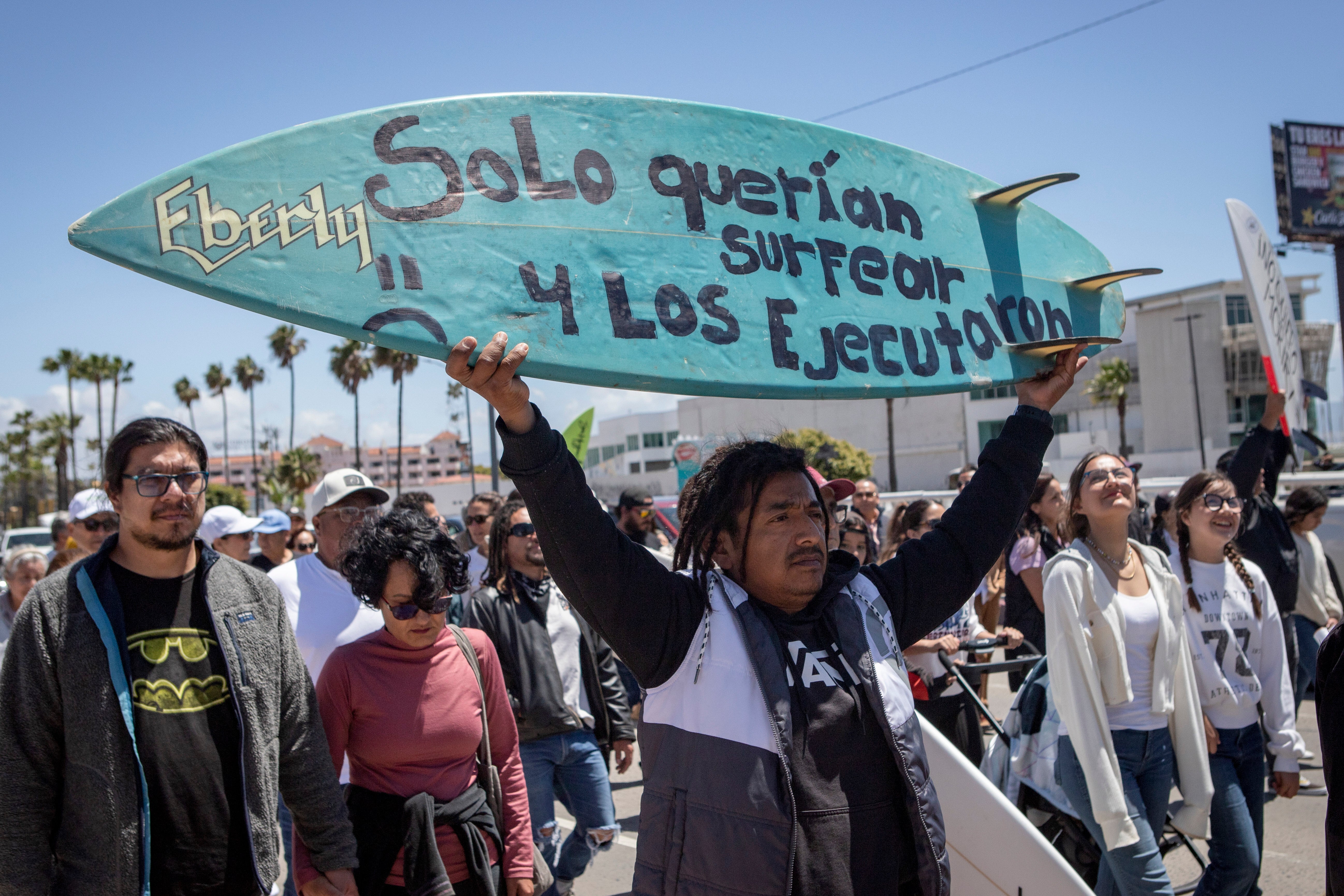 Un manifestante sostiene una tabla de bodyboard con la inscripción en español “Solo querían surfear y los ejecutaron”
