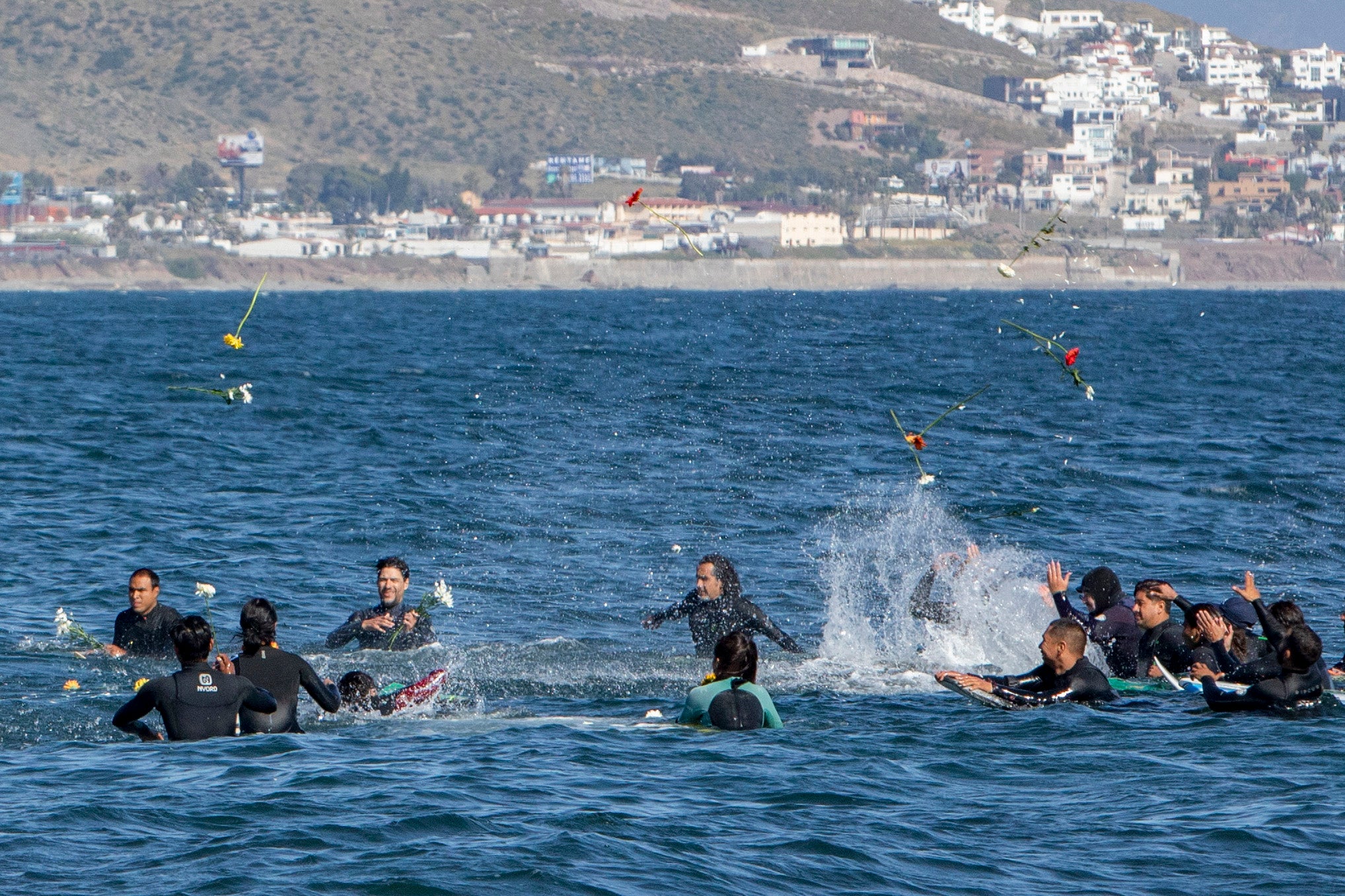 Surfistas lanzan flores durante un homenaje a remo a los tres surfistas fallecidos el domingo en Ensenada, México