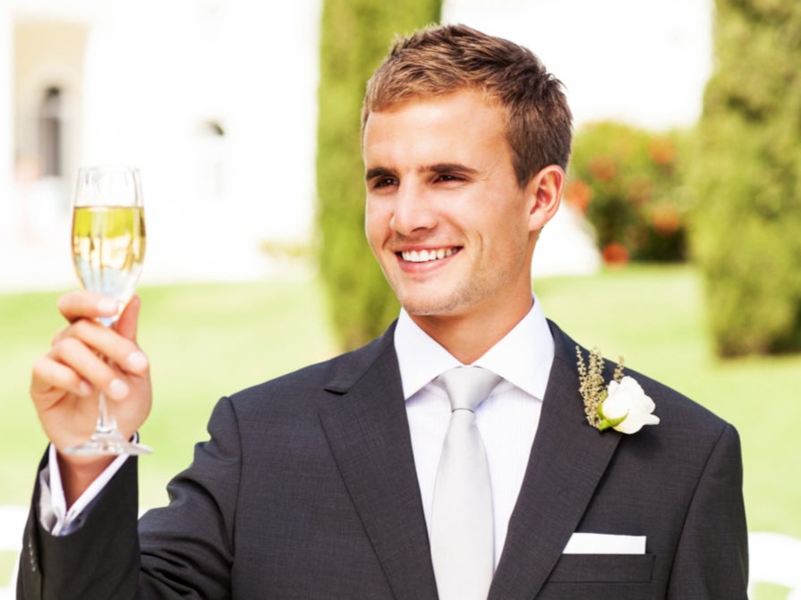 Un padrino sonríe y brinda con una copa de champán en una boda ( Getty Images )