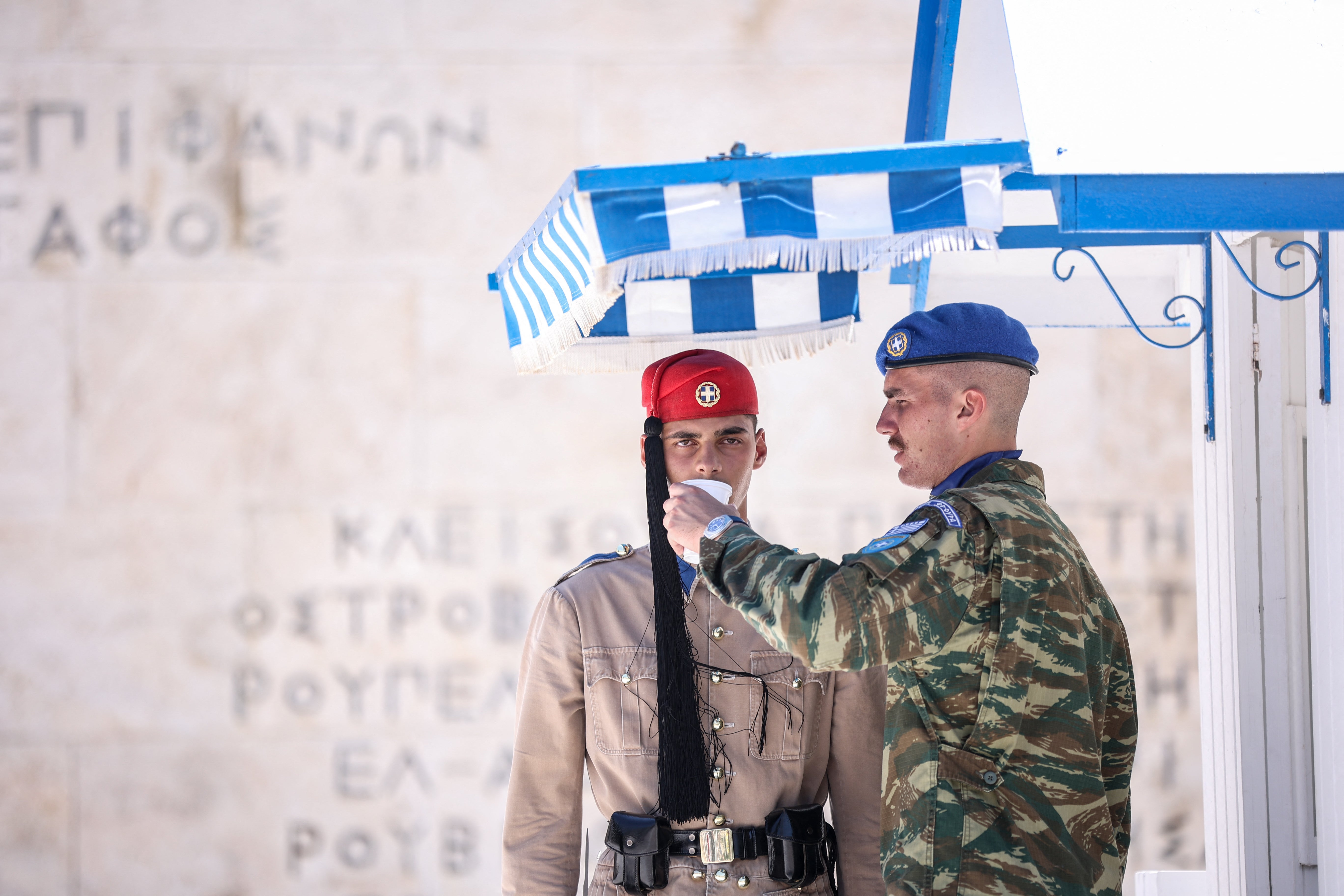 Un oficial le da agua a un miembro de la guardia presidencial frente al Monumento al soldado desconocido en la plaza Sintagma de Atenas el 12 de julio de 2024